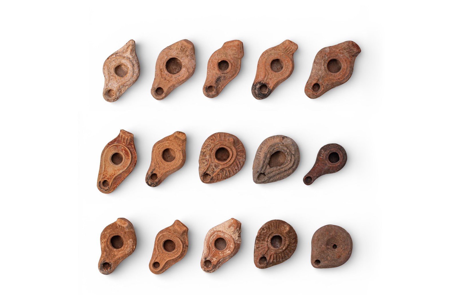 COLLECTION OF BYZANTINE TERRACOTTA OIL LAMPS: Ca. AD 300 - 600. A collection of 15 terracotta oil lamps, each leaf-shaped with a central filling hole and a rounded nozzle, with a rear lug handle of triangular or rectangular profile, some with mou