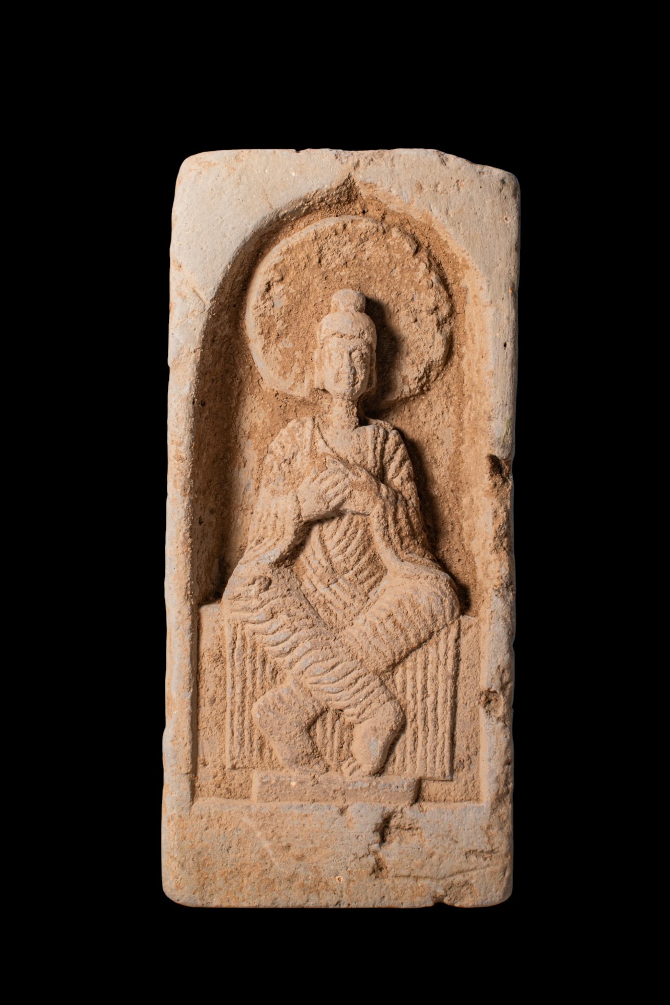 CHINESE TERRACOTTA BRICK WITH SEATED BODHISATTVA: Northern Wei dynasty, Ca. AD 386 - 535. A terracotta rectangular brick moulded in relief with a seated bodhisattva within a recessed niche framed by a pointed arch. The figure is depicted with the han