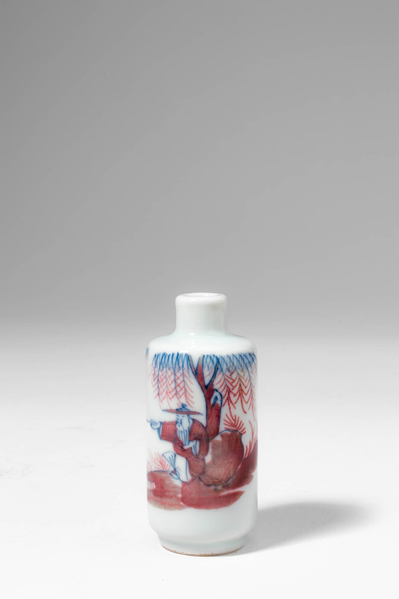 CHINESE SNUFF BOTTLE WITH UNDERGLAZE BLUE AND COPPER RED, DEPICTING A SCHOLAR IN LANDSCAPE SCENE: Qing Dynasty, Ca. AD 1644 - 1912. >A porcelain snuff bottle of elegant cylindrical form with a short, upright neck, decorated in a harmonious combination of underglaze cobalt blue and copper-red on a 