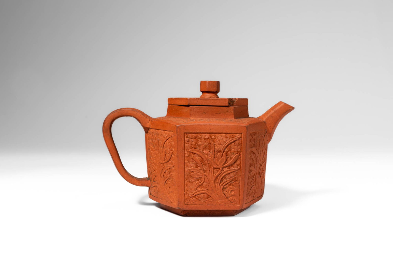 CHINESE YIXING HEXAGONAL TEAPOT WITH MOULDED DECORATION: Kangxi Period, Qing Dynasty, Ca. AD 1661 - 1722. >A Yixing stoneware teapot of hexagonal section, the straight-sided body rising from a slightly splayed base and fitted with a flat cover surmounted by