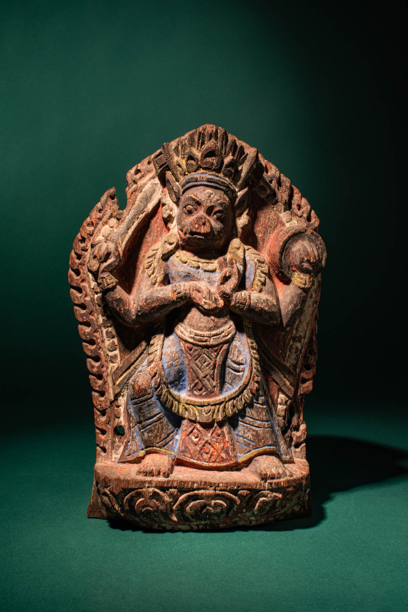 NEPALESE WOODEN SCULPTURE OF VARAHI: Ca. 17th century AD. >A carved wooden figure depicting the goddess Varahi, shown seated frontally within a foliate aureole. The deity is portrayed with a boar?s head and a robust human body, her expre