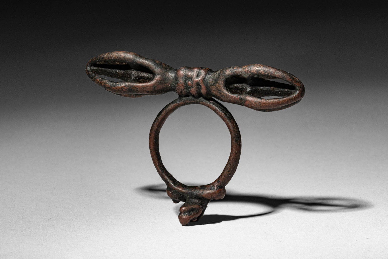 BRONZE VAJRA RING WITH WRATHFUL HEAD AND SNAKE: Dali Kingdom, Ca. 12th century AD. >A cast bronze ring combining a vajra form with an integral ring handle. Stylised vajra prongs extend horizontally from the head and curve inward at the terminals, w