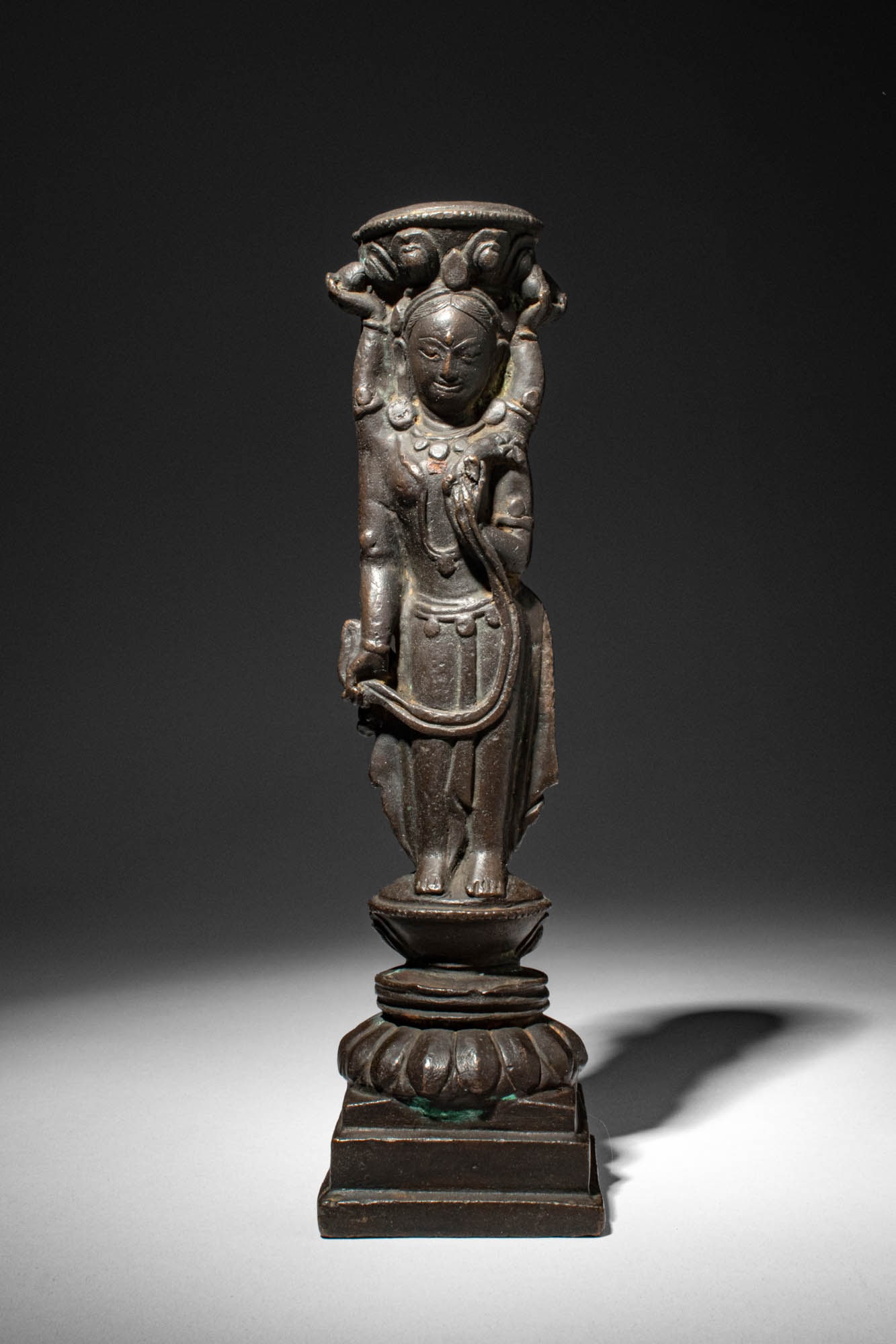 TIBETAN COPPER ALLOY COLUMN SUPPORT DEPICTING AN OFFERING GODDESS: Densatil Monastery, Ca. 14th - early 15th century AD. >A cast copper alloy column support in the form of an elegantly standing offering goddess, shown frontally and raising both arms to support a circ