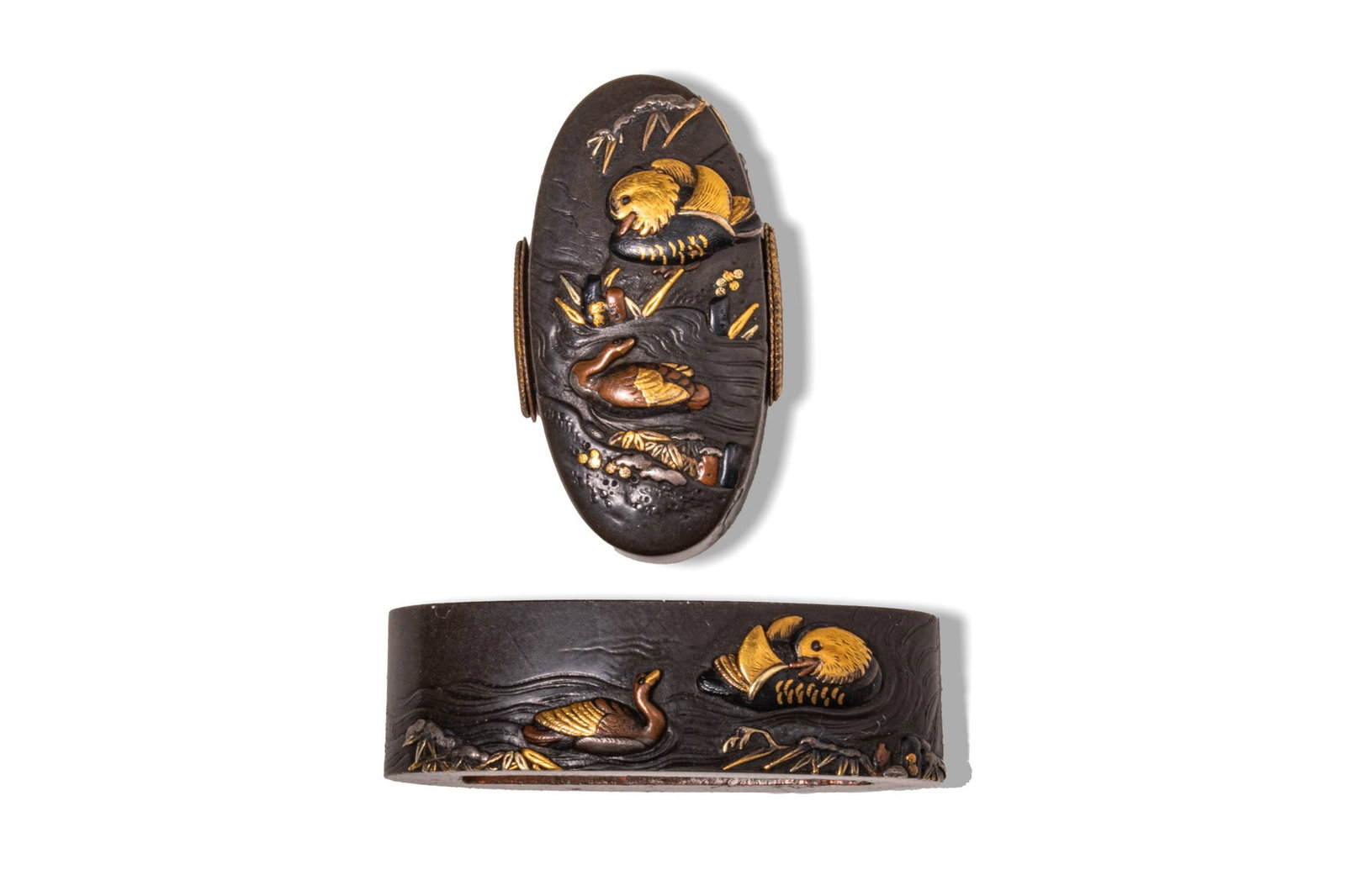 JAPANESE SHIBUICHI FUCHI-GASHIRA, NARA SCHOOL, SIGNED NARA EISHIN: Ca. AD 1800 - 1900. A fine shibuichi fuchi-gashira set, intricately decorated with a serene scene of mandarin ducks swimming. Size: 35-38mm x 16-20mm; Weight: 35g. Provenance: Prince collection, 1990s