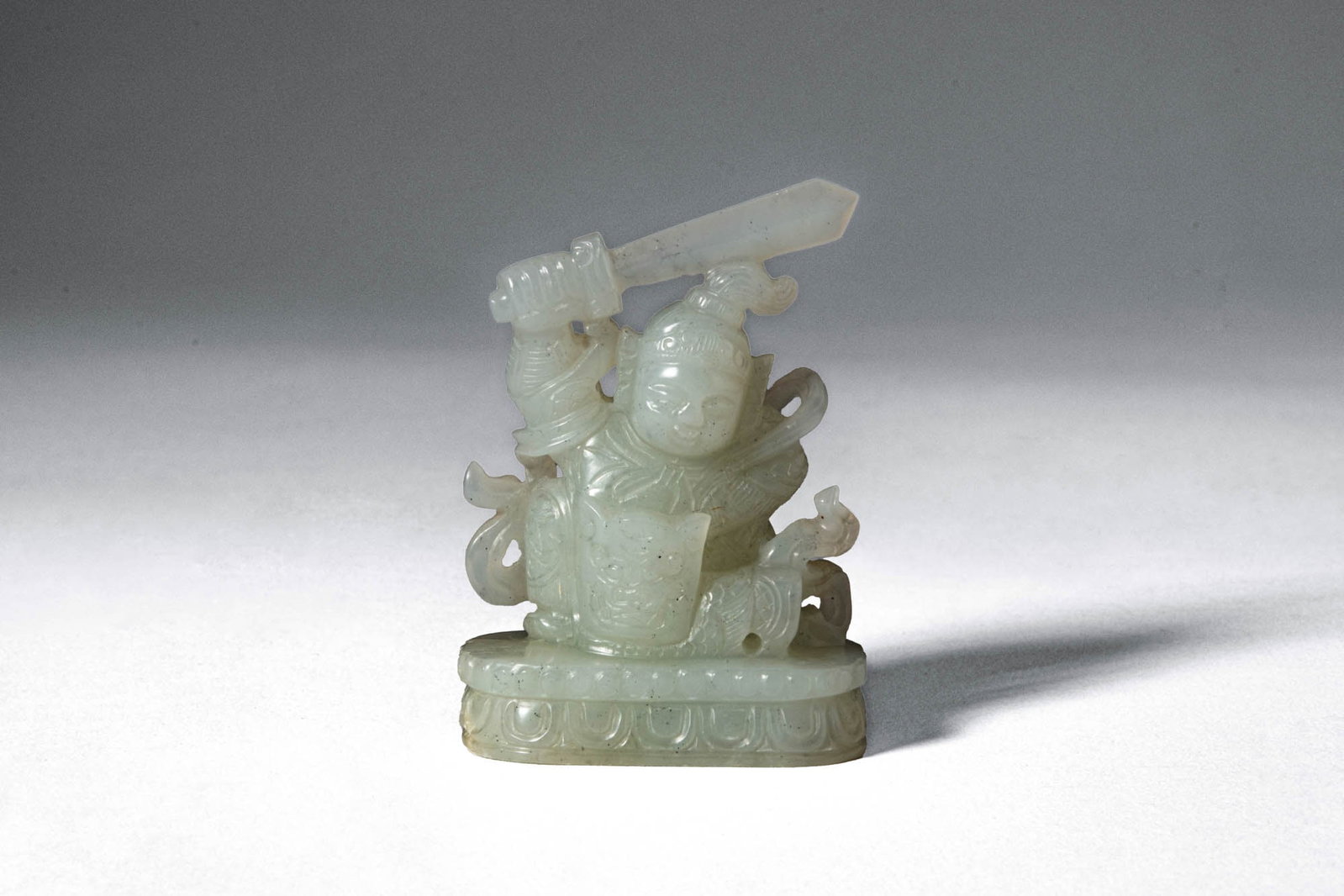 CHINESE WHITE JADE DEPICTING A WARRIOR: Mid Qing Dynasty, Ca. 18th century AD. >A finely carved white jade figure depicting a warrior seated in a composed yet alert posture, holding a sword raised across the shoulders. The figure is rendere