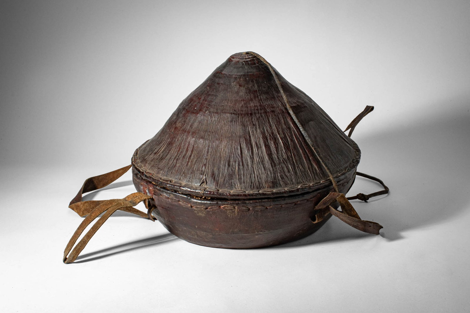 ETHIOPIAN BORANA BASKET WITH LID: Ca. late 19th - early 20th century AD. > A wooden basket and cover of domed, conical form, the lid rising to a gently pointed apex. The vessel is fitted with attachment straps and toggles, indicative 