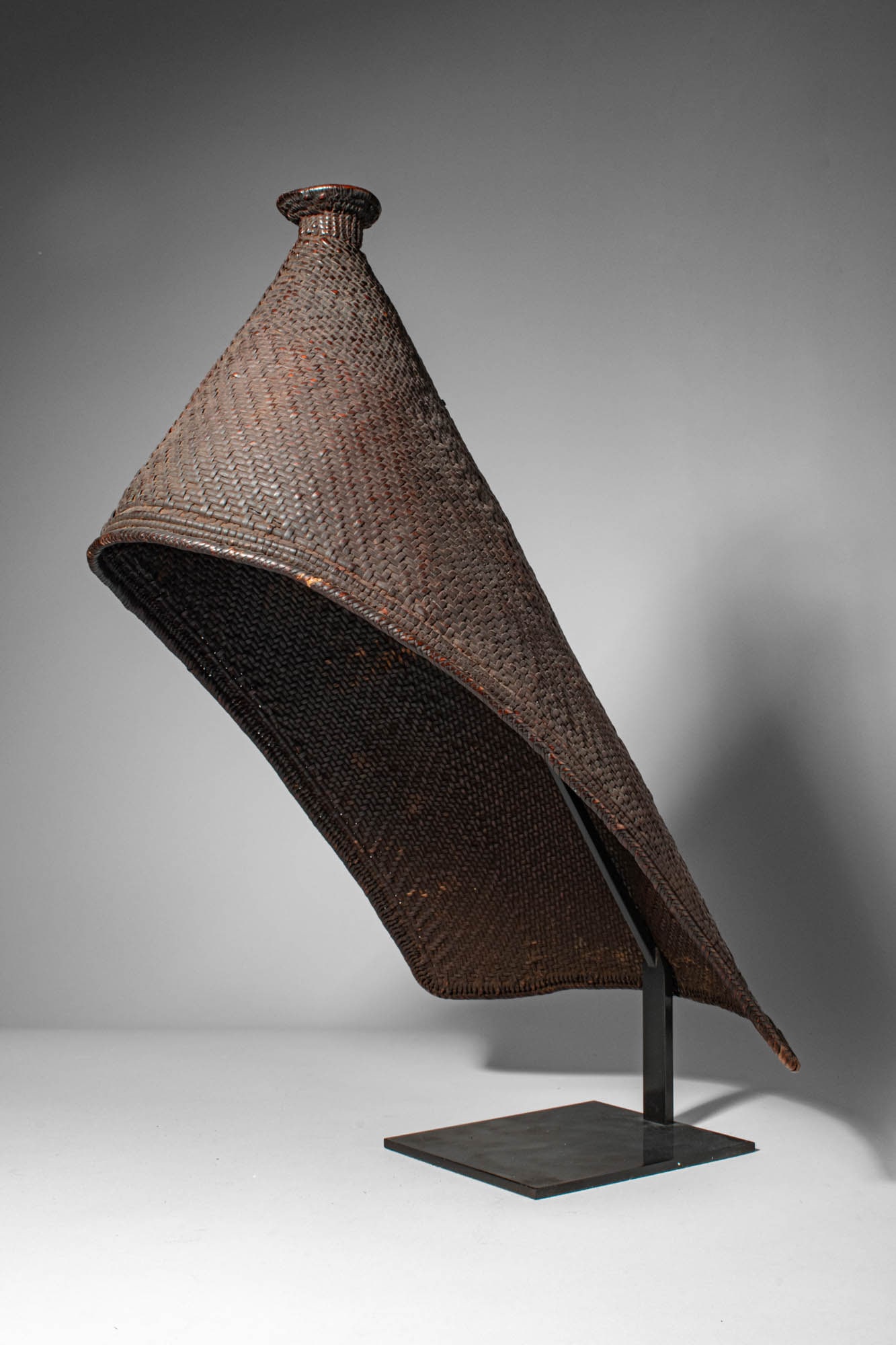MANGBETU RAIN HOOD: Ca. 20th century AD. > A finely woven Mangbetu rain hood of elongated, conical form, constructed from tightly plaited vegetal fibres. The elegant, tapering silhouette culminates in a small knop at the