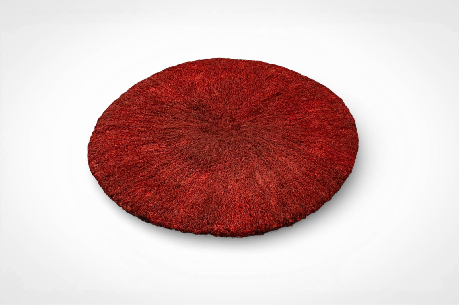 ZULU HEADDRESS: Ca. 20th century AD. >A circular Zulu hat formed from densely arranged natural fibres dyed a vivid red. The fibres radiate outward from a central point, creating a thick, textured surface and a low, d