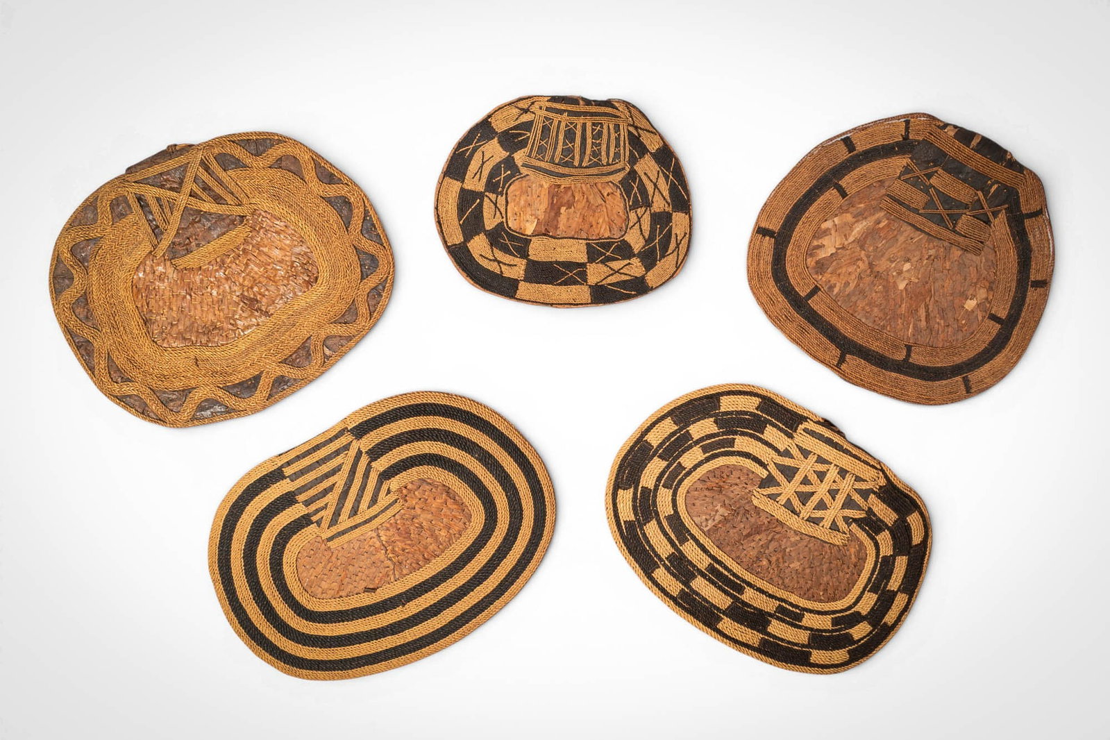 GROUP OF MANGBETU NEGBE: Ca. 20th century AD. >A group of five Mangbetu negbe, formed from bark and plant fibres and decorated with bold geometric patterns in contrasting dark and natural tones. The pieces vary in form, inclu