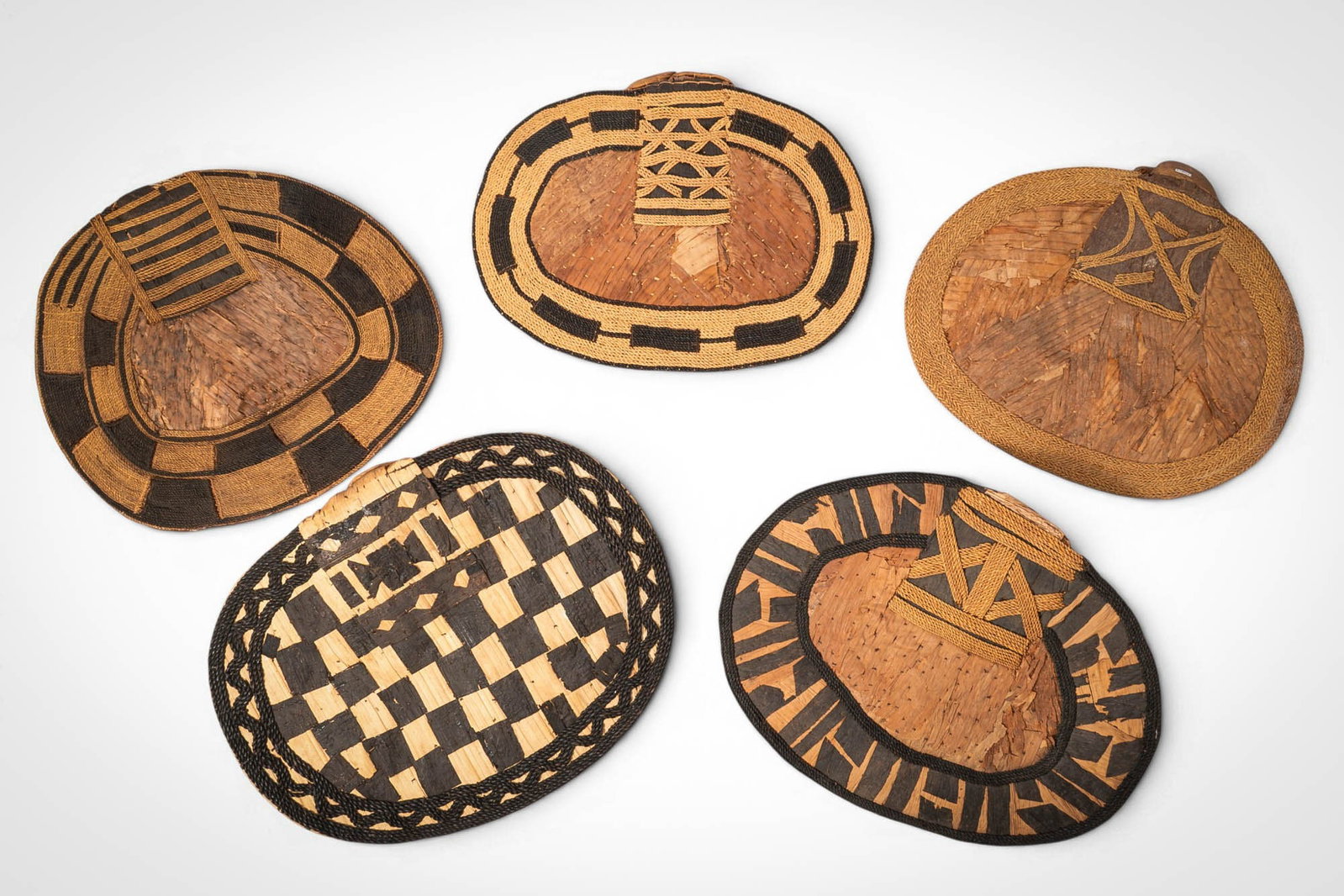 GROUP OF MANGBETU NEGBE: Ca. 20th century AD. >A group of five Mangbetu negbe, formed from bark and plant fibres and decorated with bold geometric patterns in contrasting dark and natural tones. The pieces vary in form, inclu