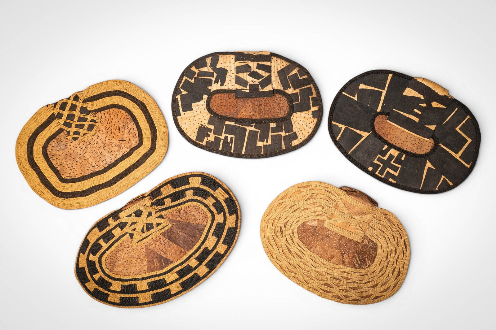 GROUP OF MANGBETU NEGBE: Ca. 20th century AD. >A group of five Mangbetu negbe, formed from bark and plant fibres and decorated with bold geometric patterns in contrasting dark and natural tones. The pieces vary in form, inclu