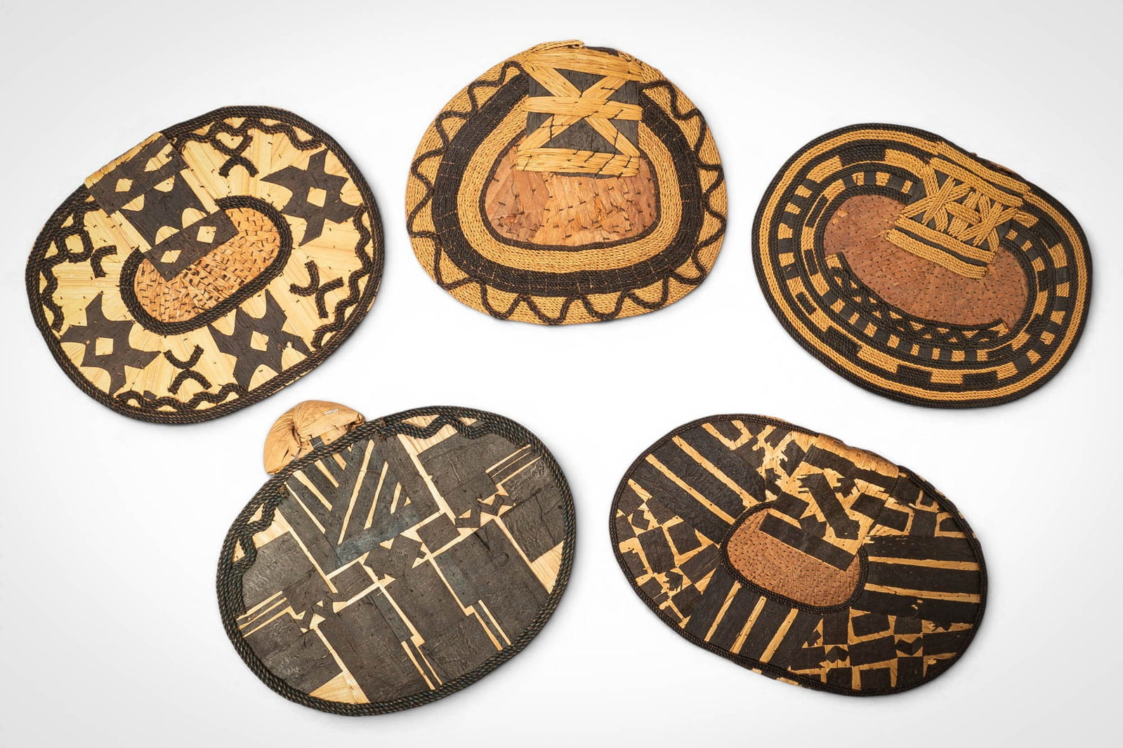 GROUP OF MANGBETU NEGBE: Ca. 20th century AD. >A group of five Mangbetu negbe, formed from bark and plant fibres and decorated with bold geometric patterns in contrasting dark and natural tones. The pieces vary in form, inclu