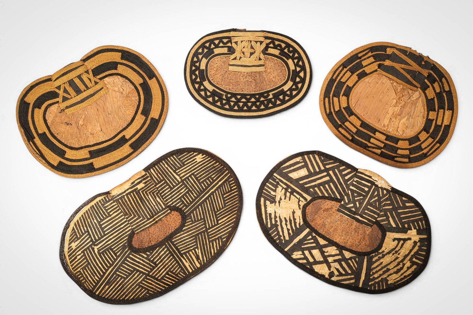 GROUP OF MANGBETU NEGBE: Ca. 20th century AD. >A group of five Mangbetu negbe, formed from bark and plant fibres and decorated with bold geometric patterns in contrasting dark and natural tones. The pieces vary in form, inclu