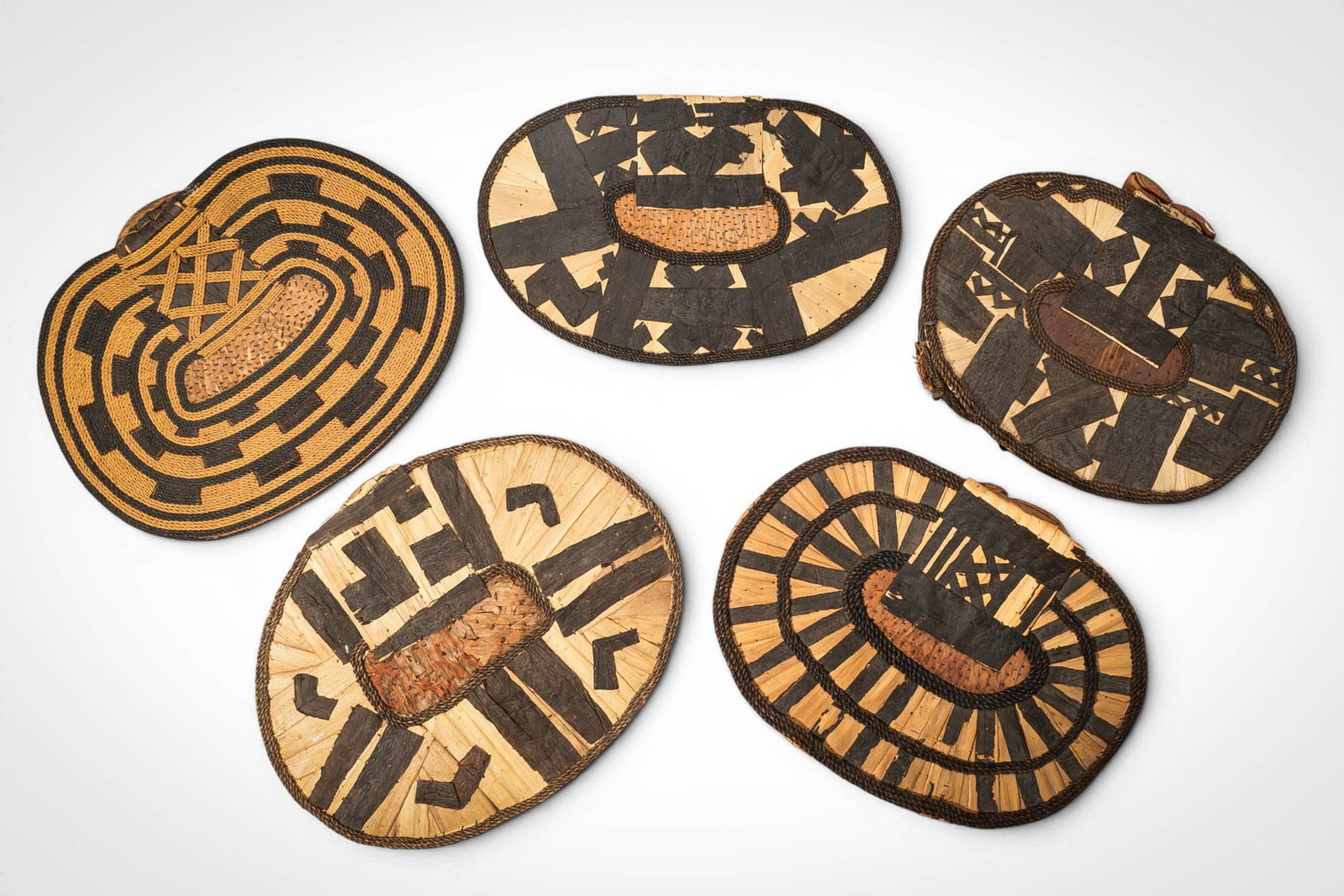 GROUP OF MANGBETU NEGBE: Ca. 20th century AD. >A group of five Mangbetu negbe, formed from bark and plant fibres and decorated with bold geometric patterns in contrasting dark and natural tones. The pieces vary in form, inclu