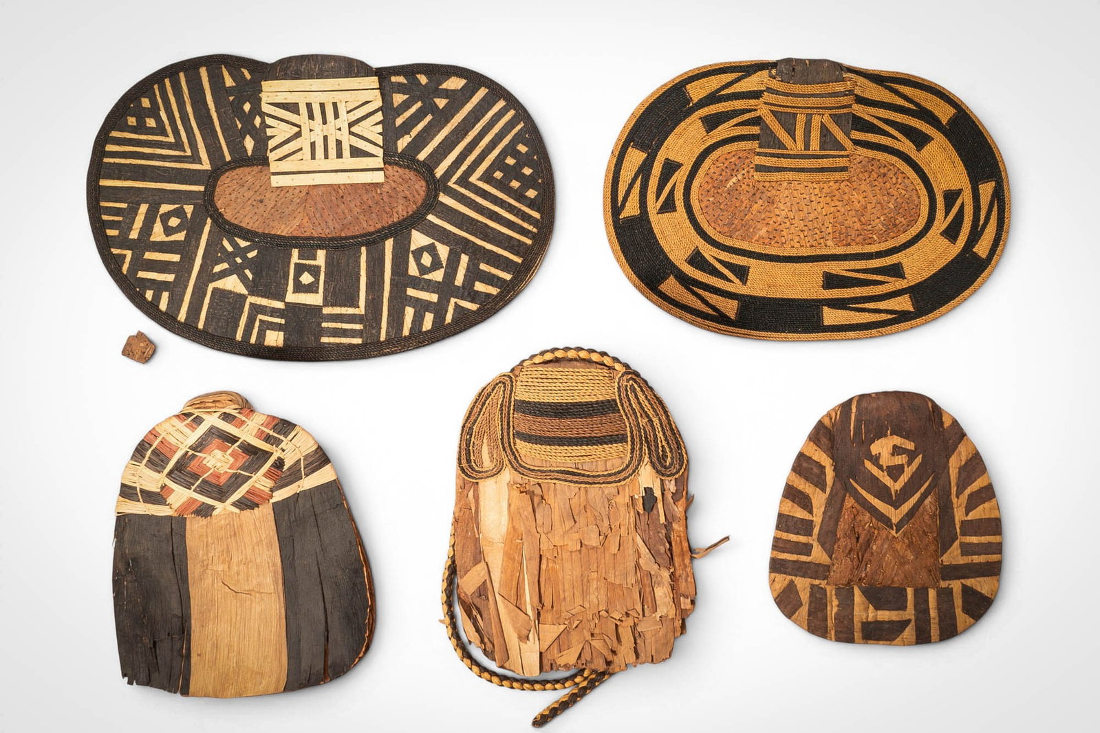 GROUP OF MANGBETU NEGBE: Ca. 20th century AD. >A group of five Mangbetu negbe, formed from bark and plant fibres and decorated with bold geometric patterns in contrasting dark and natural tones. The pieces vary in form, inclu