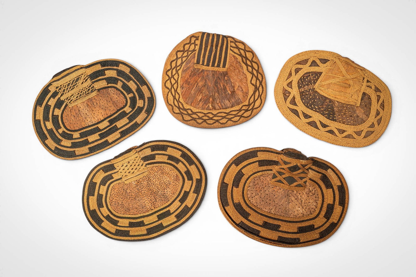 GROUP OF MANGBETU NEGBE: Ca. 20th century AD. >A group of five Mangbetu negbe, formed from bark and plant fibres and decorated with bold geometric patterns in contrasting dark and natural tones. The pieces vary in form, inclu