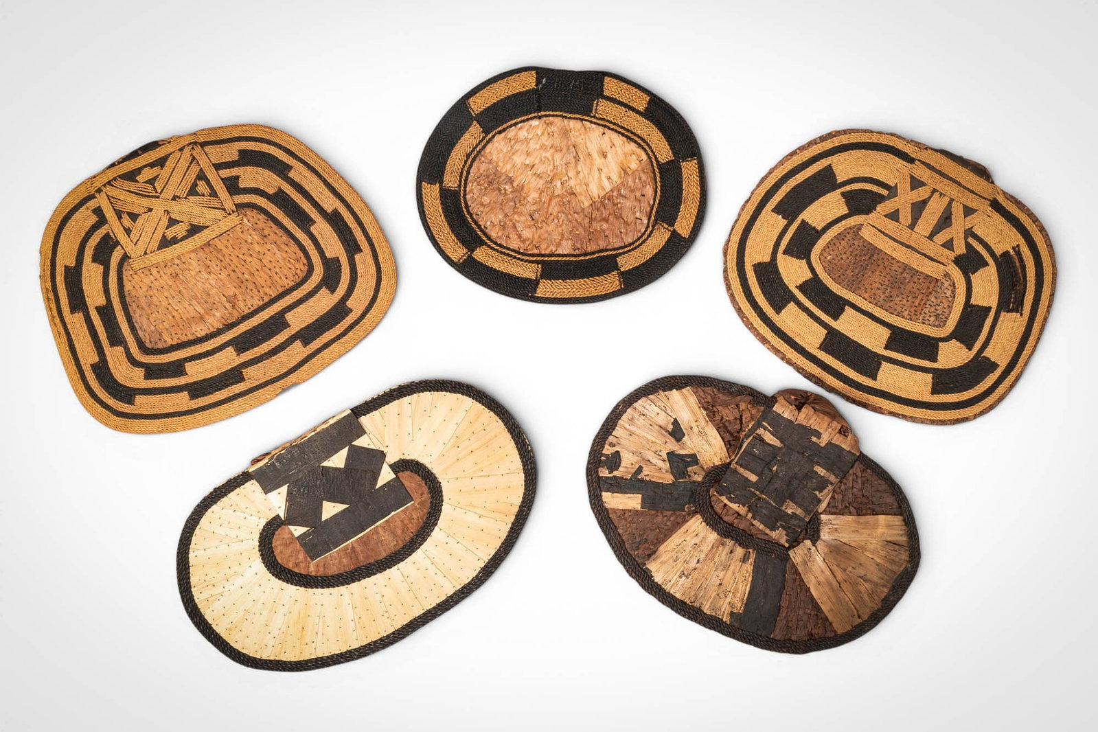 GROUP OF MANGBETU NEGBE: Ca. 20th century AD. >A group of five Mangbetu negbe, formed from bark and plant fibres and decorated with bold geometric patterns in contrasting dark and natural tones. The pieces vary in form, inclu