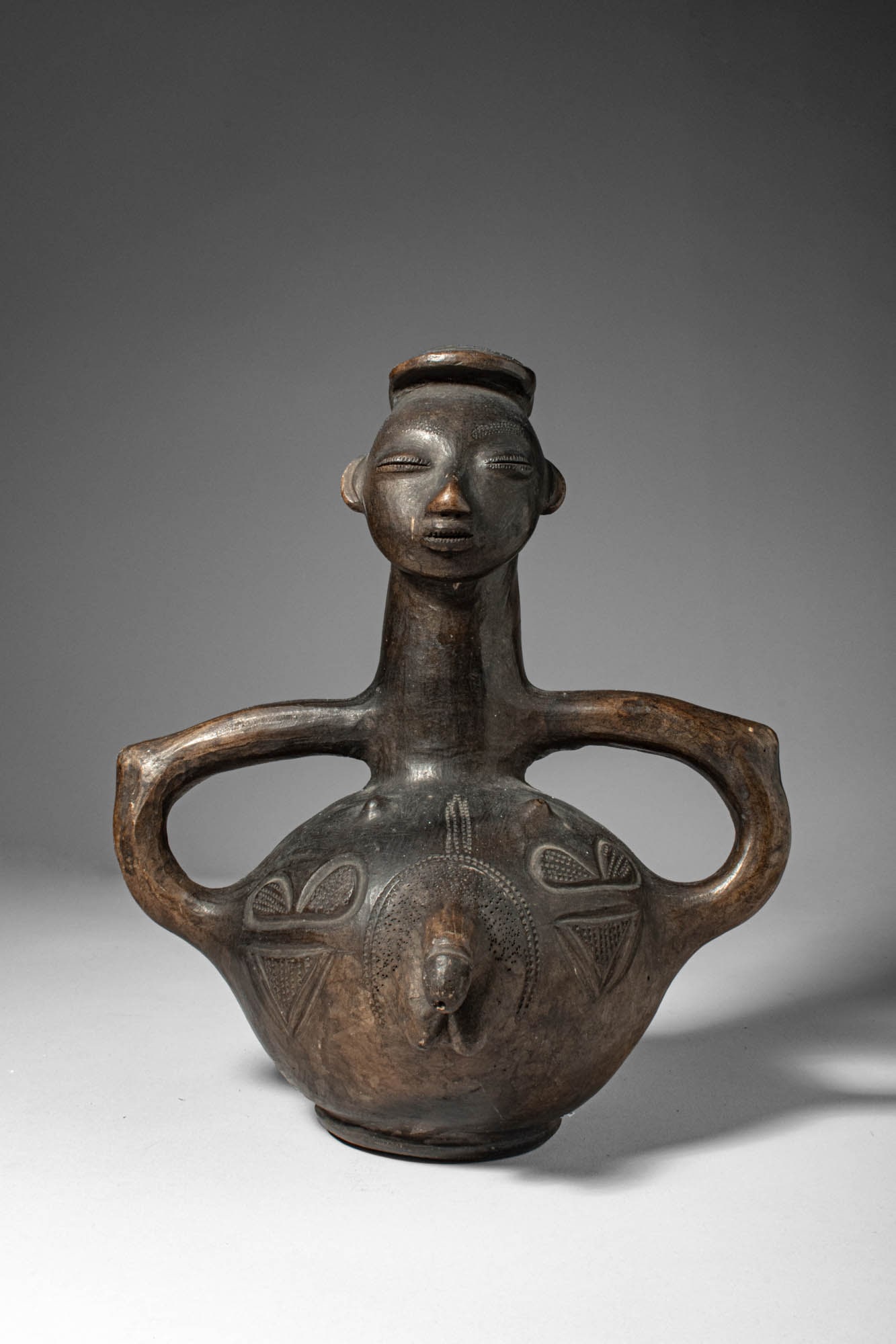 MANGBETU ANTHROPOMORPHIC TERRACOTTA VESSEL WITH ARM HANDLES: Democratic Republic of the Congo, Ca. early 20th century AD. >A finely modelled terracotta vessel of anthropomorphic form, the elongated neck rising to a serene, stylised head with characteristic Mang