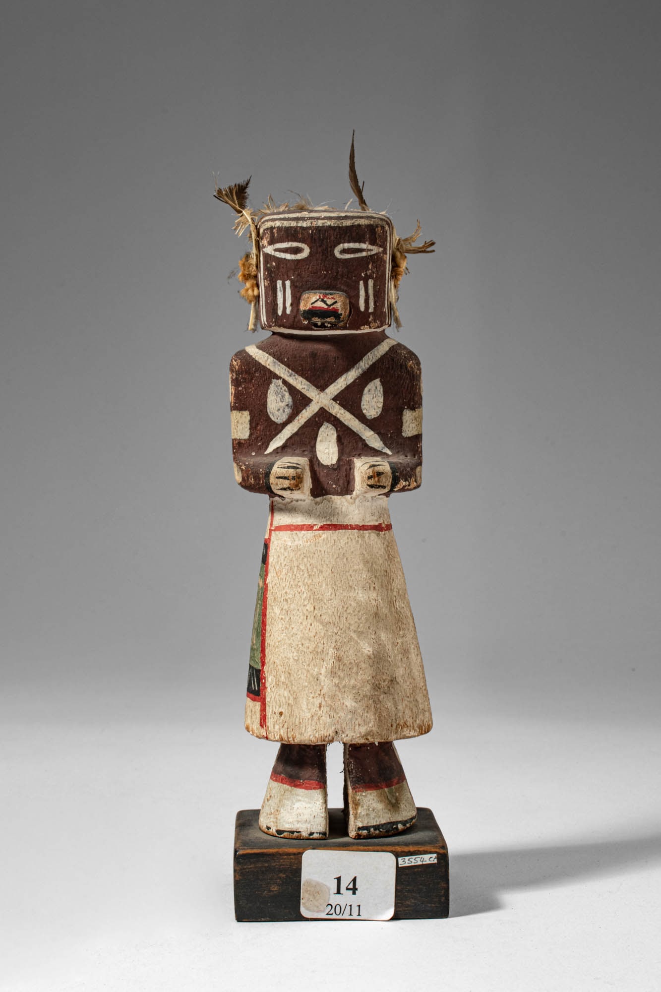 HOPI KACHINA DOLL: Ca. 20th century AD. >A standing masked figure with prominent ears, the face painted in blue, with red and yellow tunic and a black skirt with white and blue elements. The figure retains traces of pig