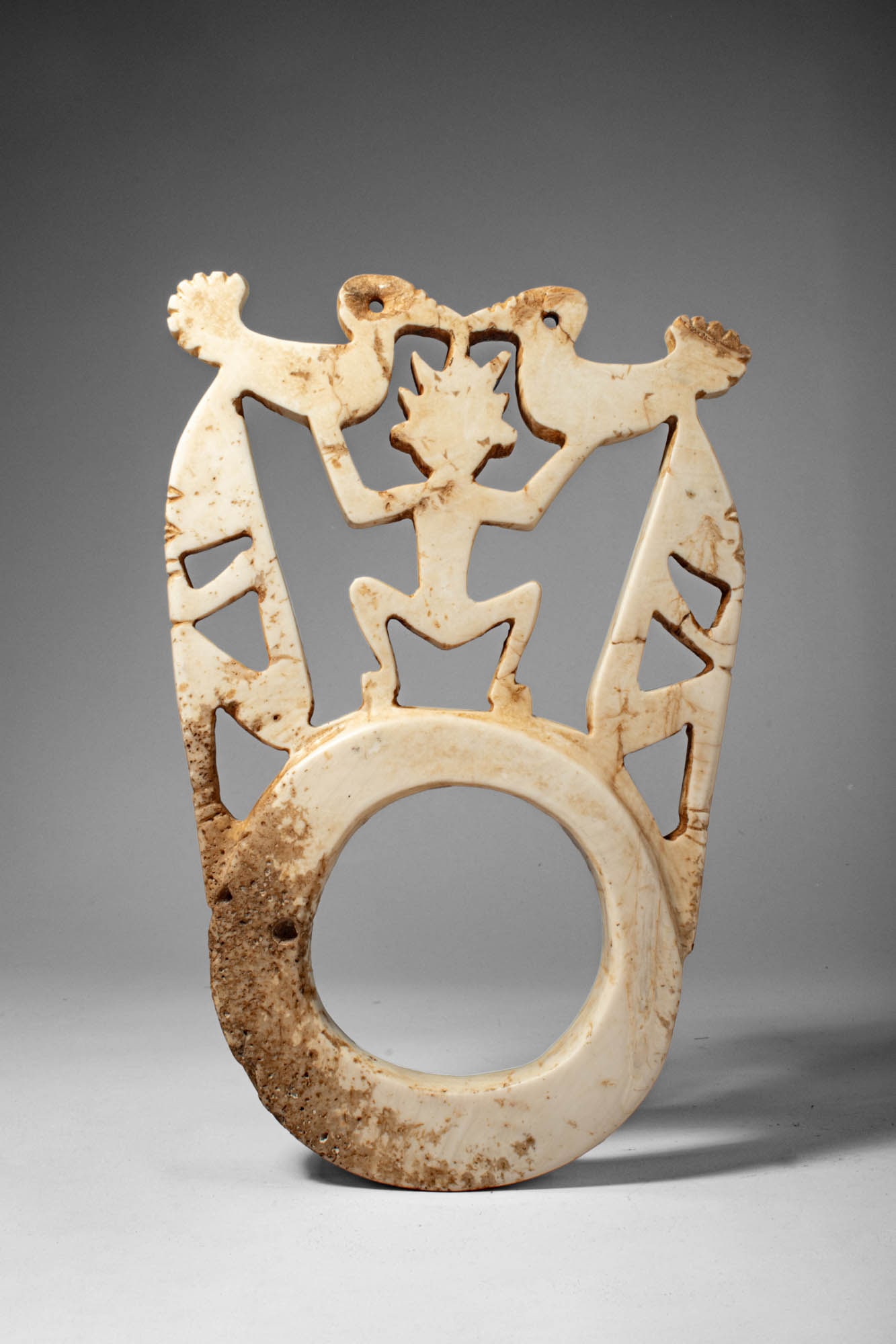 SOLOMON ISLAND BARAVA: Ca. early 20th century AD. >A pale stone openwork barava pendant features a complex figural composition above a large circular ring.The upper register depicts a stylised central human figure, shown in