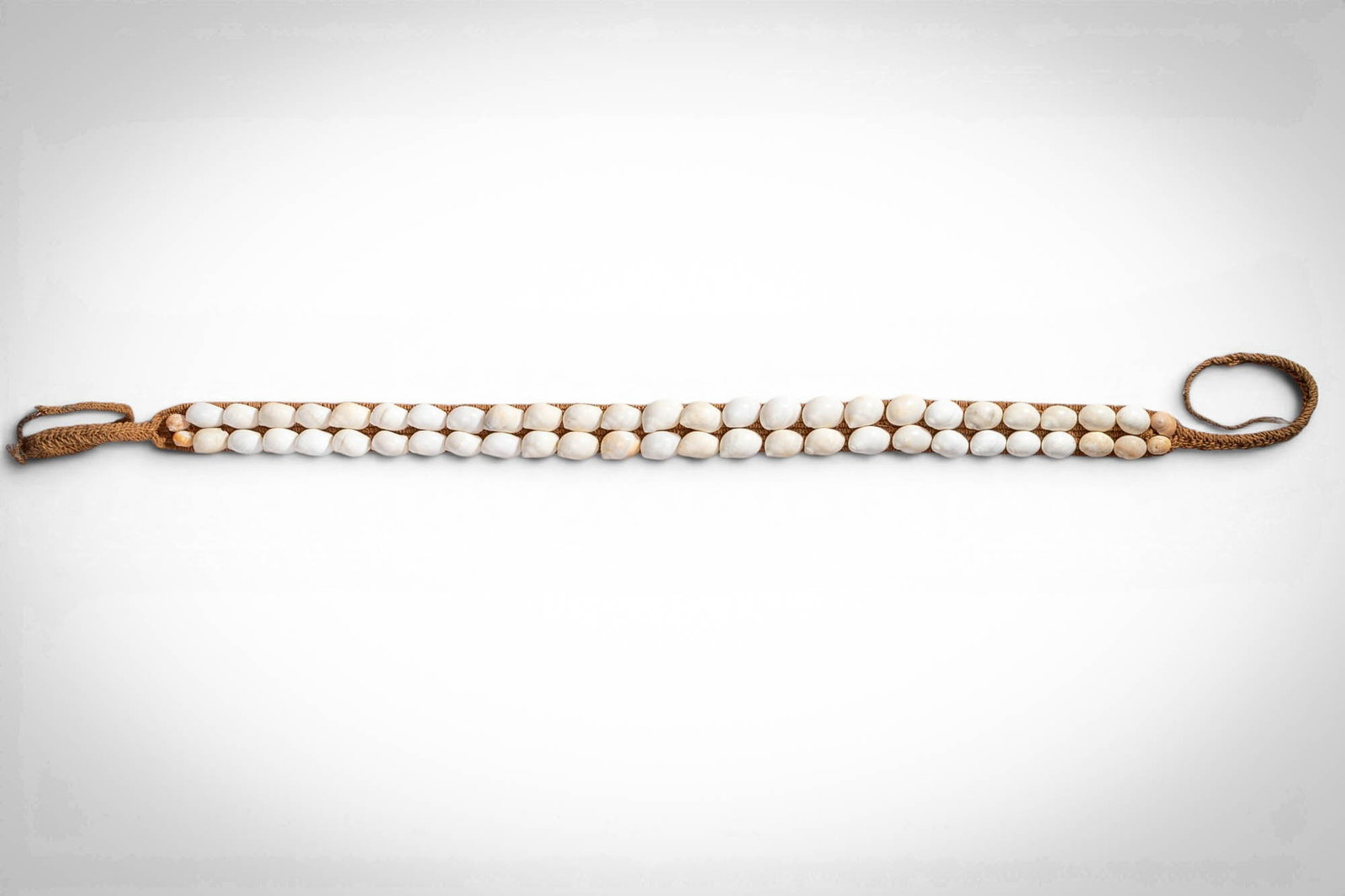MICRONESIAN YAP ISLAND WARRIOR'S BELT: Ca. late 19th - early 20th century AD. >A warrior's belt formed as a long band of plaited fibre strung with closely set white shell discs arranged in double rows, terminating in looped fibre attachmen