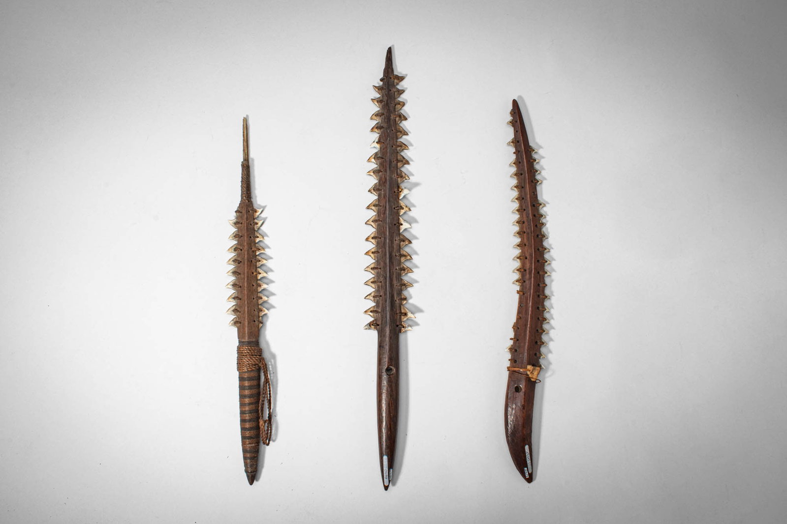 COLLECTION OF MICRONESIAN KIRIBATI WOODEN DAGGERS: Ca. 19th - 20th century AD. >A collection of three wooden daggers of elongated form, each fitted with rows of inset serrated teeth along the blade edges, secured with fibre bindings. One example retai