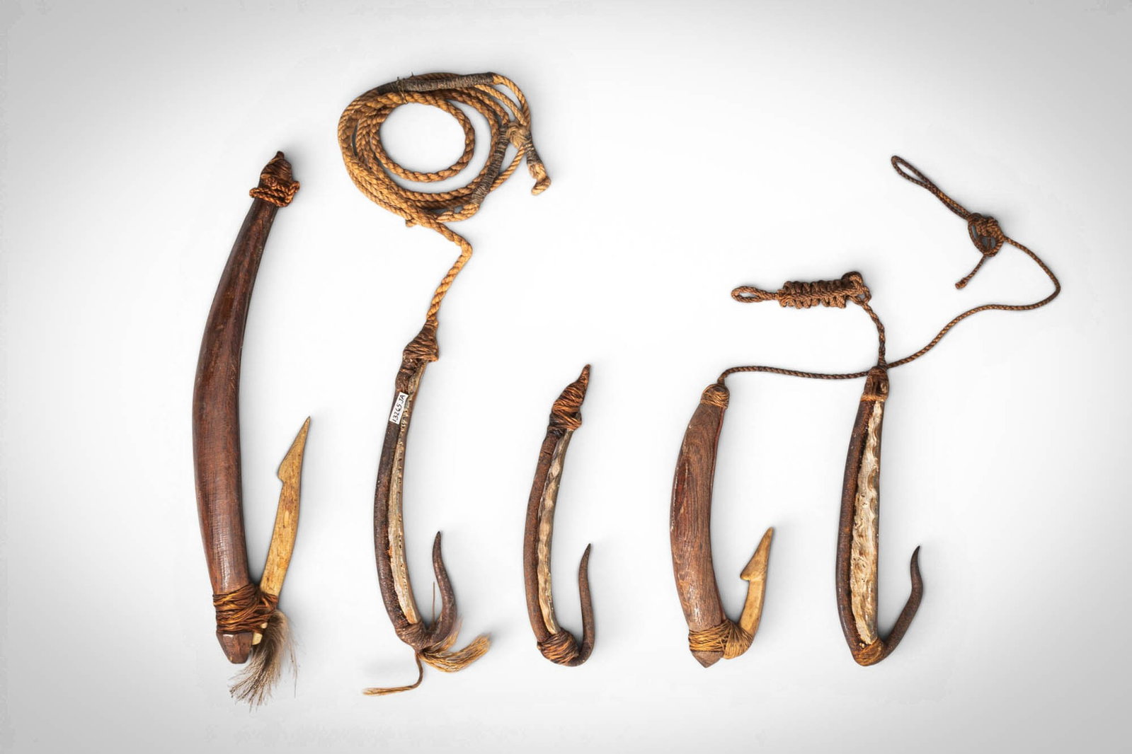 GROUP OF NEW ZEALAND MAORI FISH HOOKS: Ca. late 19th - early 20th century AD. >A group of carved fish hooks of varying size, worked in wood and bone, several of composite construction with fibre bindings and cord attachments. Each is of ch