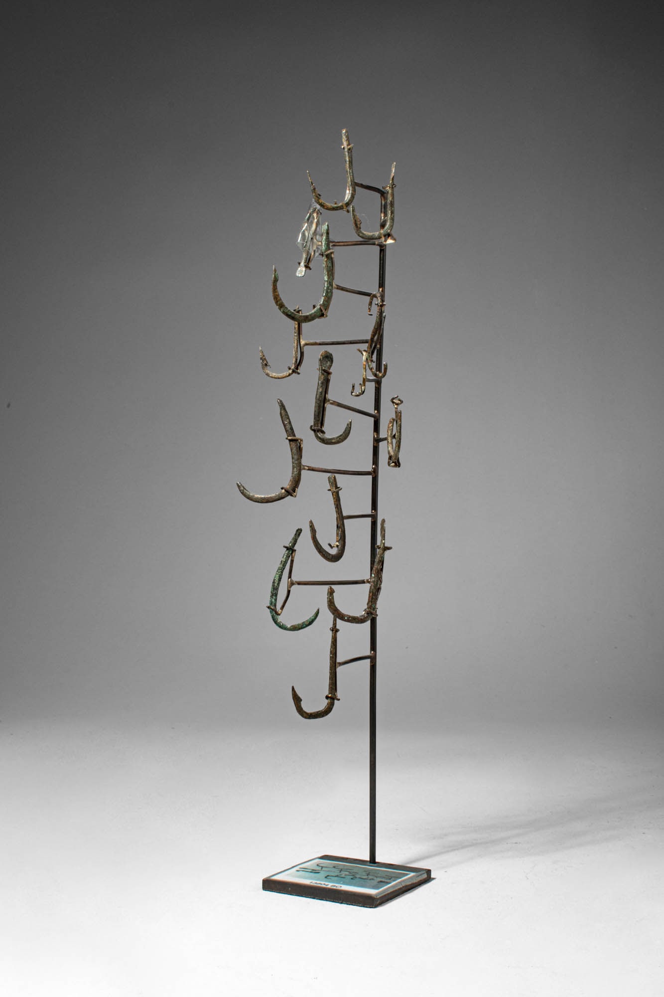 COLLECTION OF ROMAN BRONZE HOOKS: Ca. 1st century BC - 3rd century AD. >A varied group of bronze fishing hooks of differing sizes and forms, mounted for display.The assemblage includes multiple examples with curved shafts and recurved