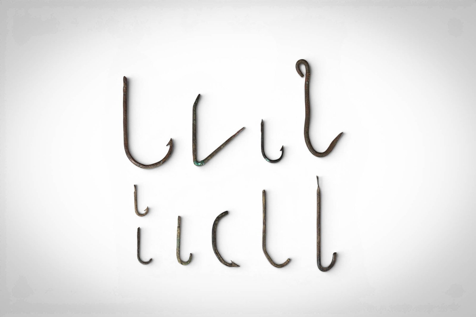 ROMAN BRONZE FISH HOOKS: Ca. 1st - 4th century AD. >A group comprising ten bronze fish hooks of varying size and form, including examples with curved shanks, barbed points, and occasional flattened or looped terminals. The su