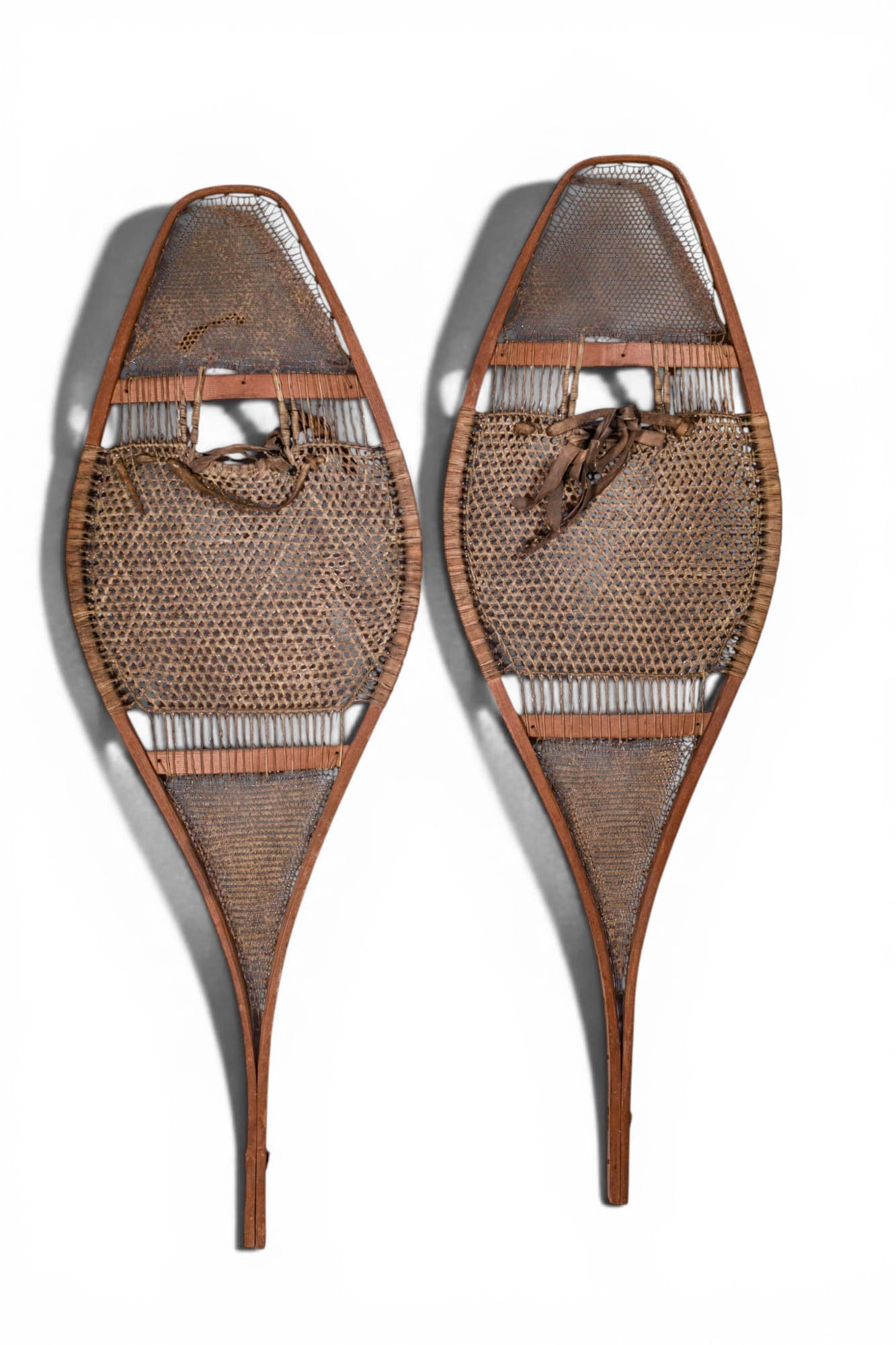 PAIR OF SNOW SHOES, NORTH AMERICAN: Ca. 19th - 20th century AD. >A matched pair of wooden snowshoes of elongated teardrop form, each with a bentwood frame enclosing finely woven rawhide webbing. The central openings are fitted with simp