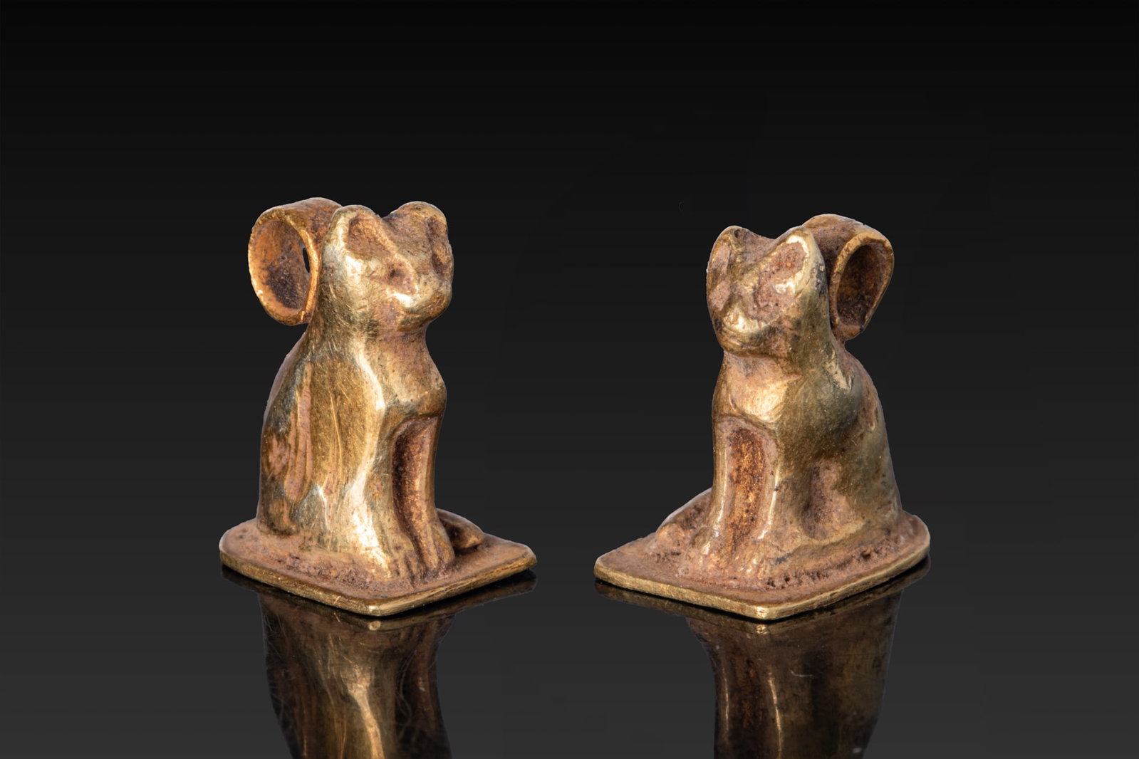 PAIR OF EGYPTIAN GOLD CAT AMULETS: Late Period, Ca. 664 - 332 BC. A pair of gold cat amulets, each modelled seated on a rectangular base with the forelegs together, and the tail curled at the side. A suspension loop rises behind the he