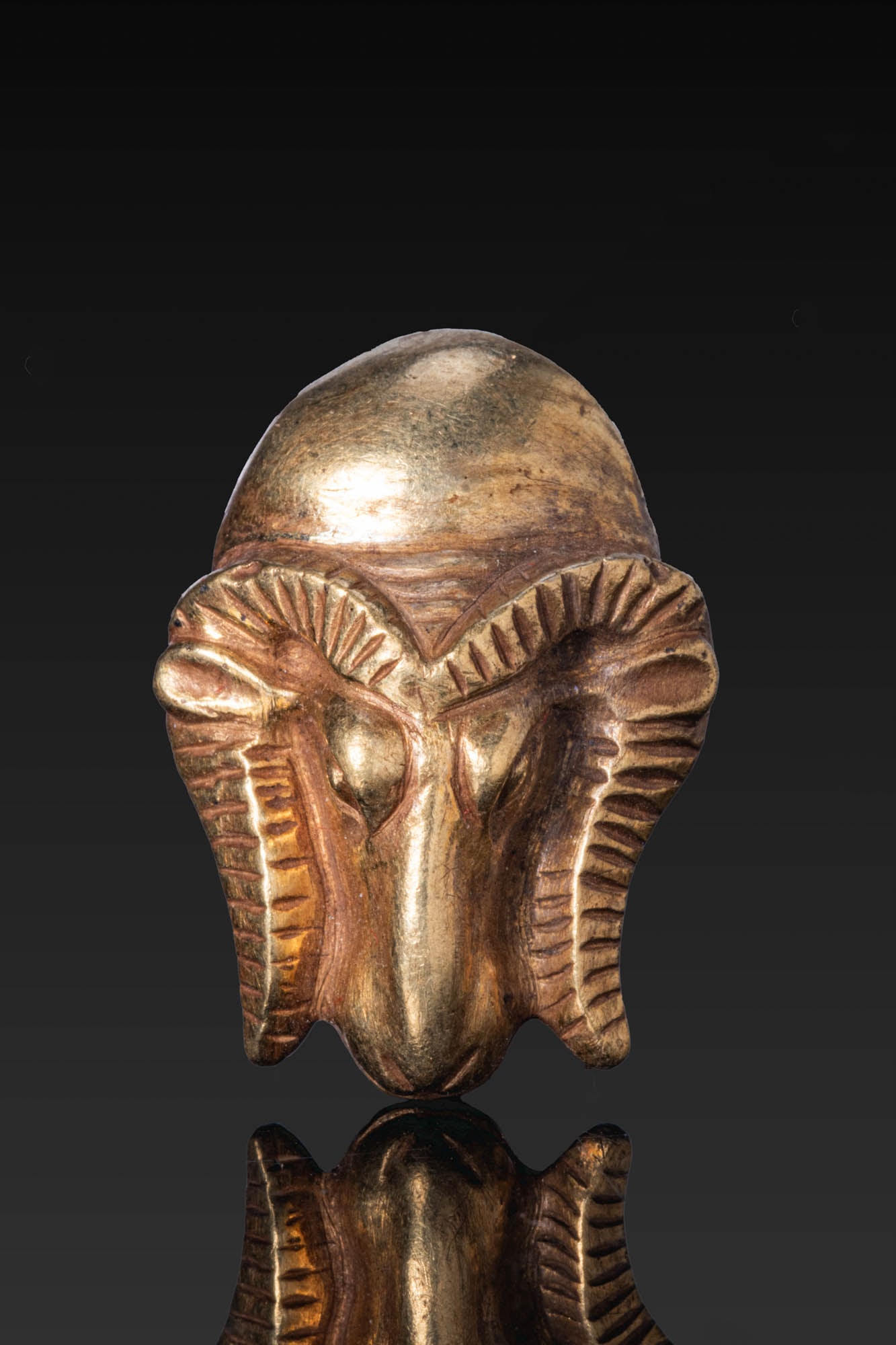EGYPTIAN PENDANT OF A RAM'S HEAD: Late Period–Ptolemaic Period (ca. 664–30 B.C.) A gold pendant of a ram's head with ribbed horns framing the face and a sun disc above. A suspension loop is attached at the back. For similar see: T