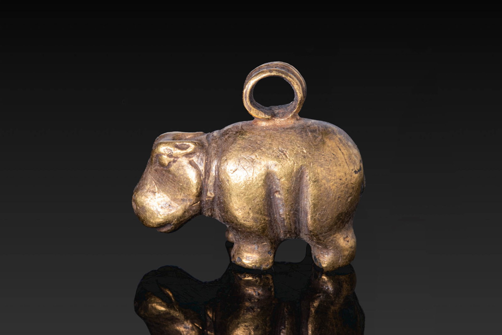 EGYPTIAN GOLD HIPPOPOTAMUS PENDANT: Middle Kingdom, Ca. 2055 - 1790 BC. A gold pendant in the form of a hippopotamus with a rounded body, short legs, and a broad head with incised eyes, mouth and nostrils. A suspension loop rises from t