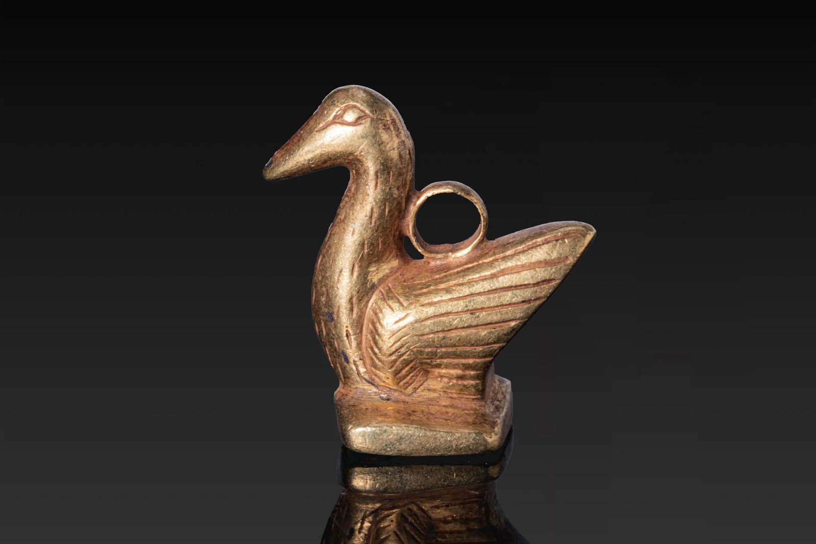 EGYPTIAN GOLD DUCK-SHAPED PENDANT: Late Period, Ca. 664 - 332 BC. A gold pendant in the form of a duck with a long neck, pointed beak, and folded wings marked with incised lines, on a rectangular base engraved underneath. A suspension 