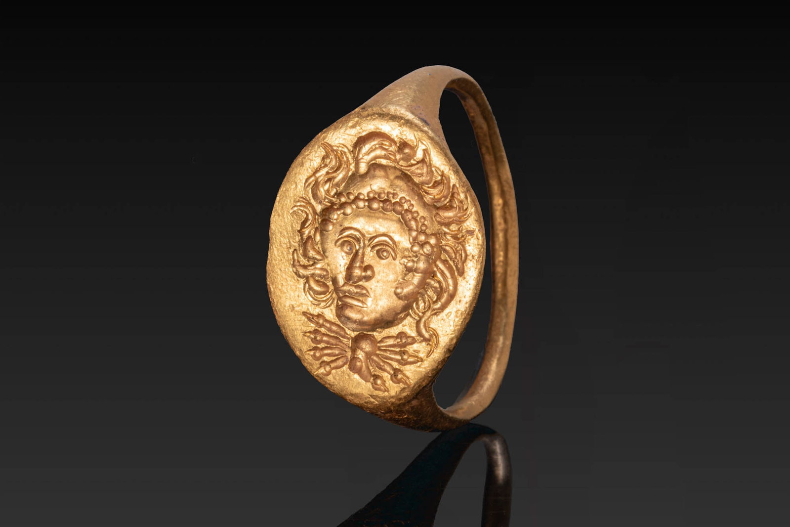 HELLENISTIC GOLD RING WITH ALEXANDER THE GREAT AS HERAKLES: Ca. 300 - 100 BC. A gold ring with a slender hoop expanding to an oval bezel engraved with the head of Alexander the Great depicted as Herakles, with the lion's mane around the face and over the brow,