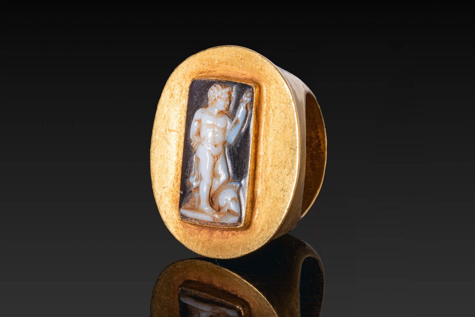 HEAVY ROMAN GOLD RING WITH CAMEO OF MARS WEARING A CORINTHIAN HELMET: Ca. 100 - 27 BC. A gold ring with a broad, rounded hoop and an oval bezel plate set with a rectangular cell containing a cameo carved with Mars standing nude, with a Corinthian helmet at his feet. For
