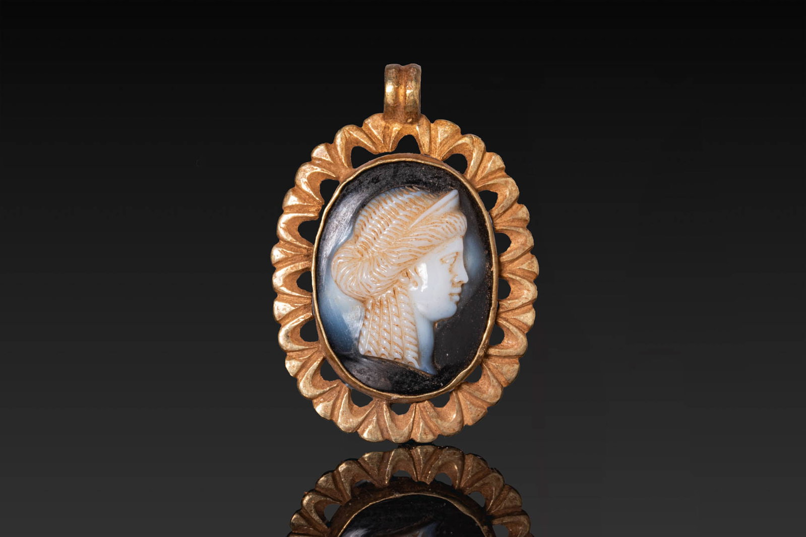 ROMAN GOLD PENDANT WITH AGATE CAMEO OF HELLENISTIC QUEEN: Ca. 100 BC - AD 100. A gold pendant of oval form, with an openwork border of radiating petal-shaped lobes, set with an oval agate cameo carved with the profile bust of a Hellenistic queen facing right