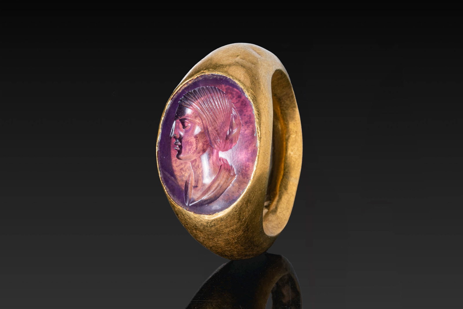 ROMAN GOLD RING WITH AMETHYST INTAGLIO OF JULIA DOMNA: Ca. AD 200 - 210. An amethyst intaglio engraved with the bust of Julia Domna in left profile, her hair drawn back into a striated coiffure, set in a possibly later gold ring with a broad, rounded hoop