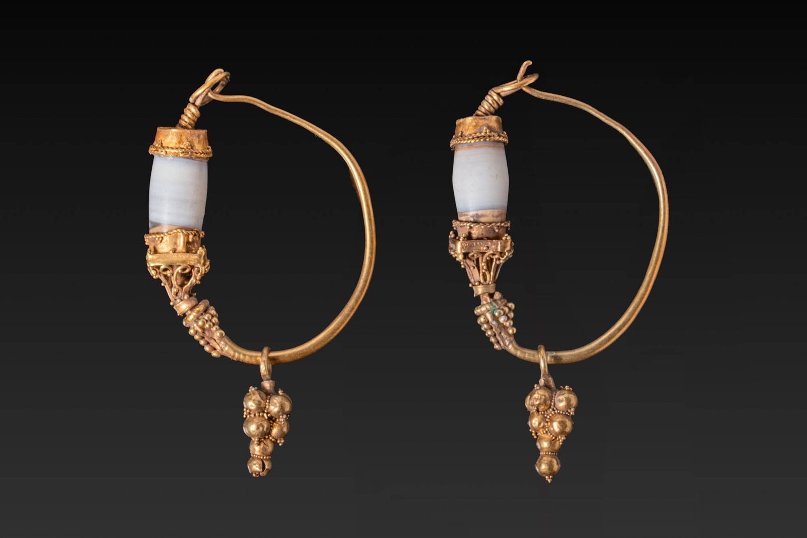 MATCHED PAIR OF GRAECO-ROMAN GOLD EARRINGS WITH AGATE BEADS AND GRANULATED DROPS: Ca. 300 - 100 BC. A matched pair of gold earrings, each with a tapering round-section hoop with a hooked terminal fastening through a loop at the opposite end. Below the loop is a tubular agate bead s