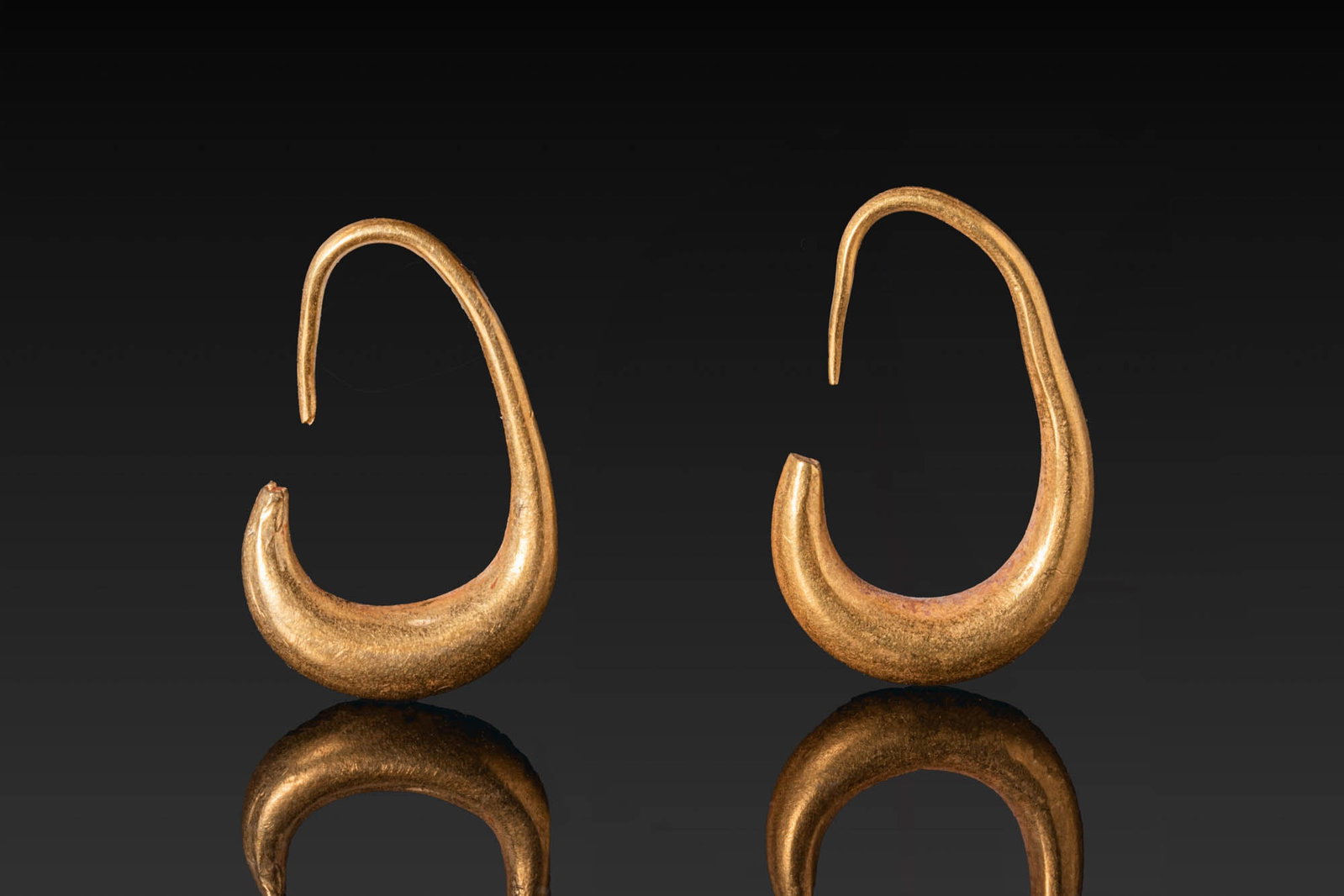 MATCHED PAIR OF CANAANITE GOLD LUNATE-SHAPED EARRINGS: Ca. 1500 BC. A matched pair of gold lunate-shaped earrings, each formed as a hollow crescent with an elongated hook above. For similar see: The Israel Museum, Jerusalem, Accession number: 92.17.185. S