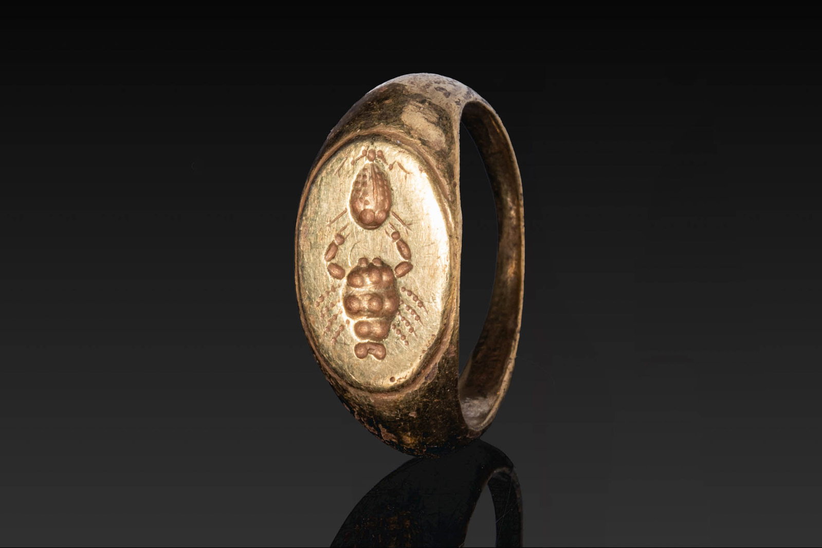 ROMAN SOLID HIGH KARAT GOLD RING WITH CRAB: Ca. AD 1 - 300. A high karat gold ring with a broad flat hoop expanding to an oval bezel engraved with a crab, with a stylised motif above. Size: D:17.32mm / US: 7 / UK: N 1/2; Weight: 7.4g Provenance