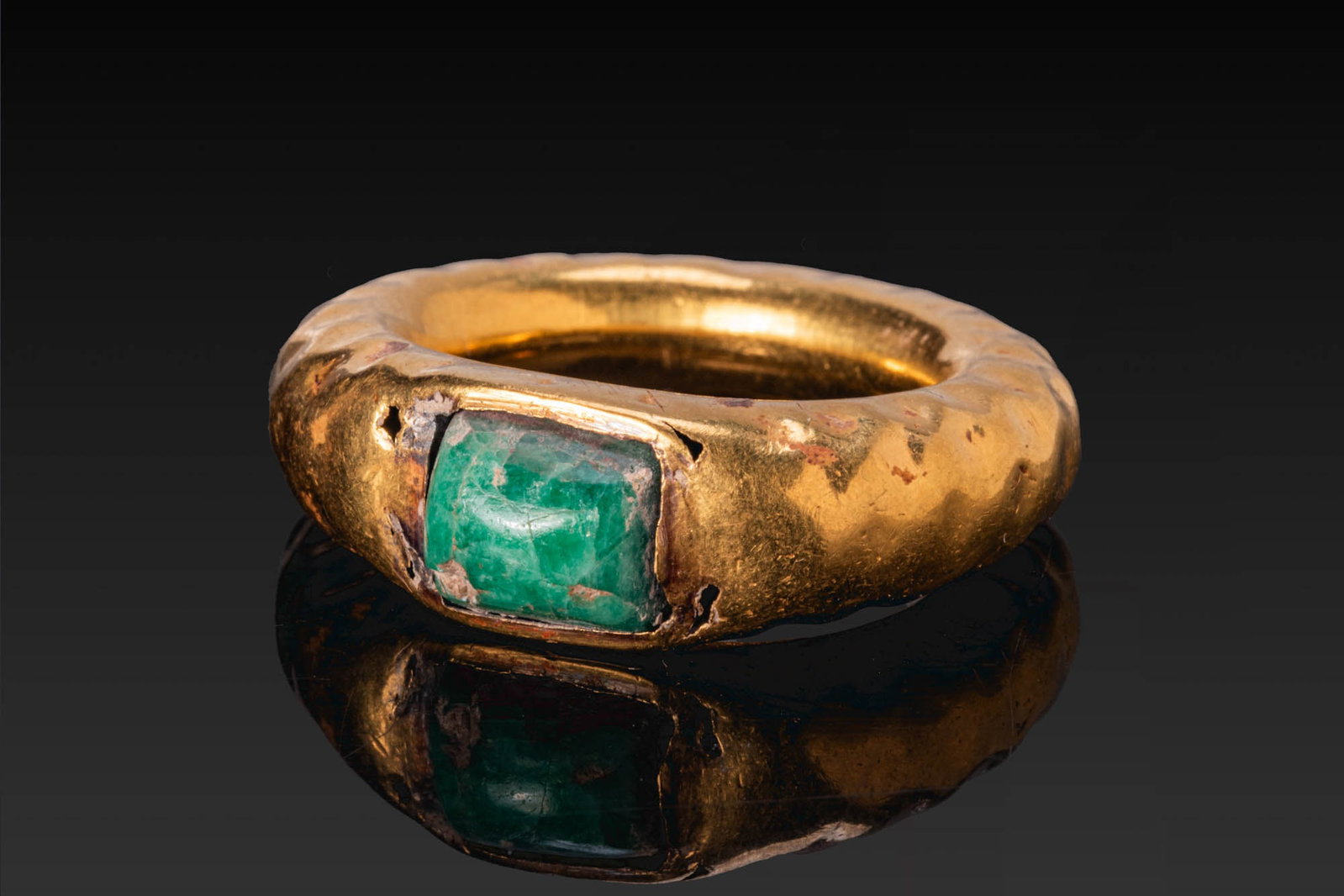 LATE ROMAN GOLD RING WITH RECTANGULAR EMERALD: Ca. AD 400 - 600. A gold hollow ring with a broad, rounded hoop and a rectangular bezel set with a rectangular emerald in a plain mount. For a similar cabochon, see: The British Museum, Museum number