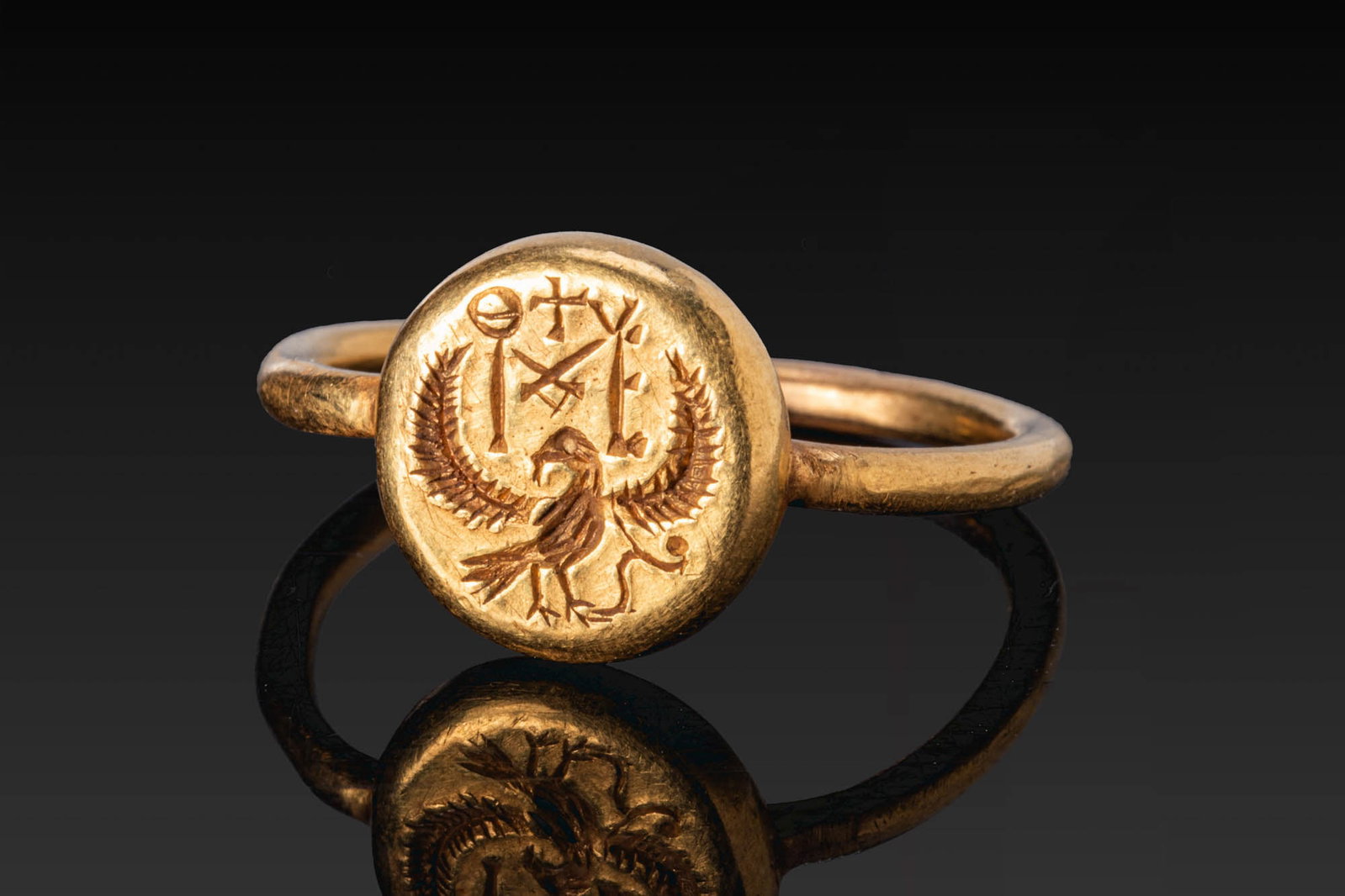 LATE ROMAN GOLD RING WITH EAGLE AND MONOGRAM: Ca. AD 600. A gold ring with a plain round-section hoop and a circular bezel engraved with an eagle with outspread wings, with a monogram above. Size: D:19.15mm / US: 9 1/4 / UK: S; Weight: 7.7g
