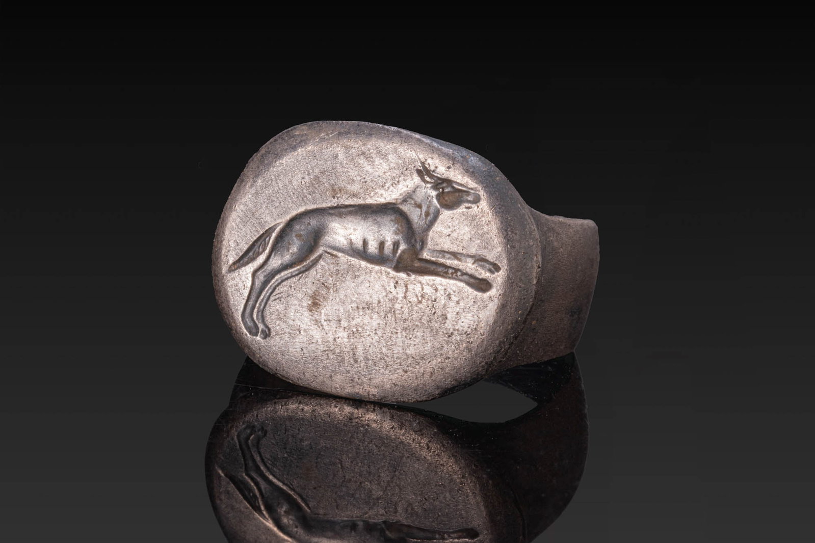 ROMAN SILVER RING WITH A HOUND: Ca. AD 1 - 50. A silver ring with a flat-section hoop widening towards an oval bezel engraved with a hound leaping to the right. For similar see: The Classical Art Research Centre, Record Number: