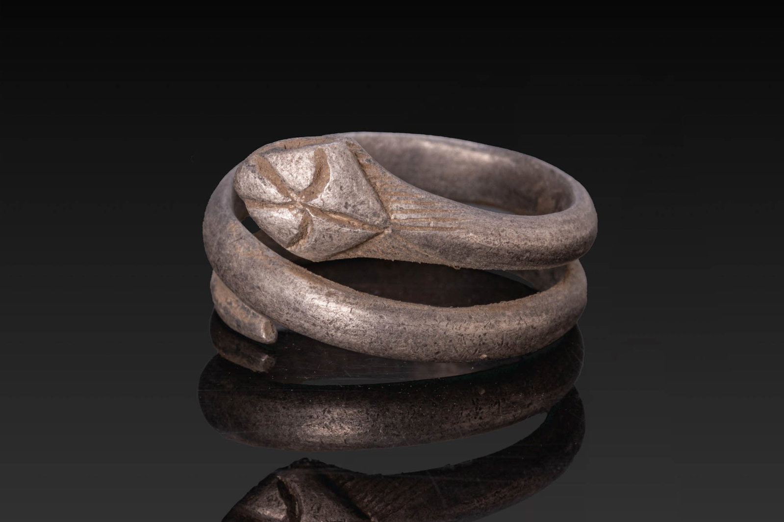 ROMANO-BRITISH SILVER SNAKE RING: Ca. AD 1 - 100. A silver snake ring formed as a spiralling hoop of D-section coiling in two turns around the finger. One end terminates in a flattened head with incised lines, and the other in a