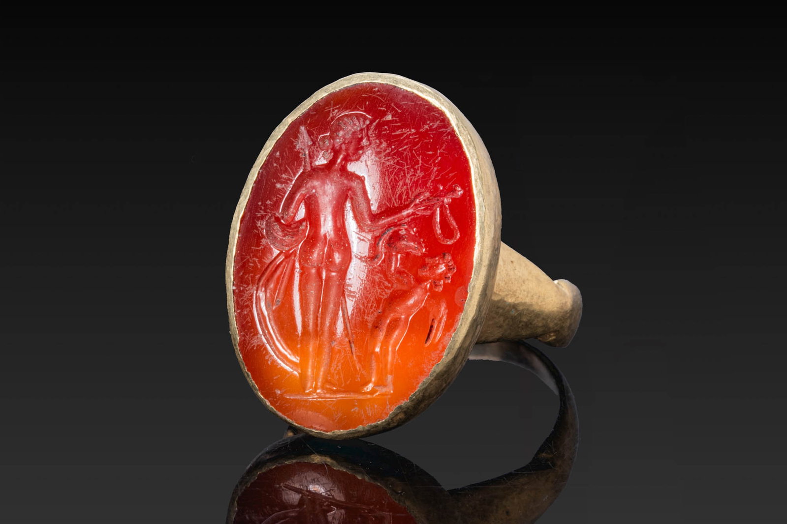 ROMAN CARNELIAN INTAGLIO OF VENUS VICTRIX AND CUPID IN GOLD RING: Ca. AD 50 - 200. A carnelian intaglio engraved with Venus Victrix, standing to the right with the body seen from behind, holding a long spear, shield and drapery in her left hand and a sword in her