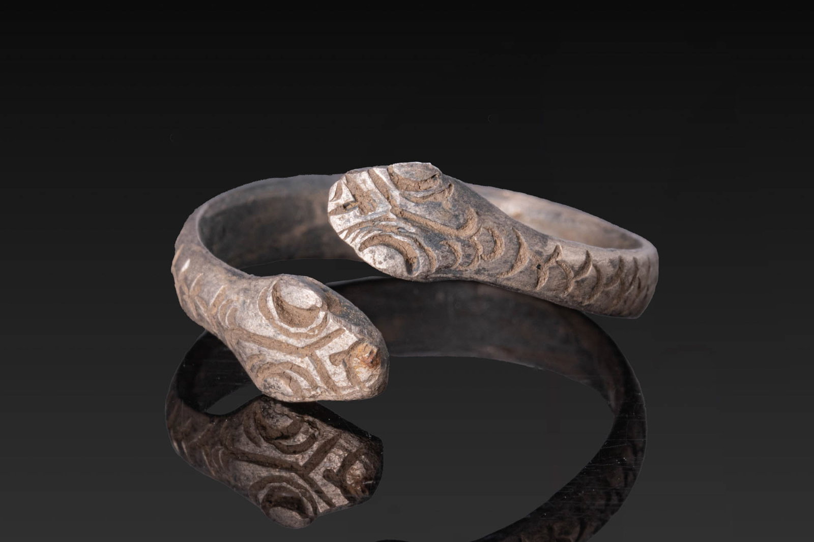 ROMANO-BRITISH SILVER SNAKE RING: Ca. AD 1 - 200. A silver ring formed as an open flat-section hoop, each end broadening into a stylised snake head with incised facial features and scales along the exterior. For similar see: The Briti