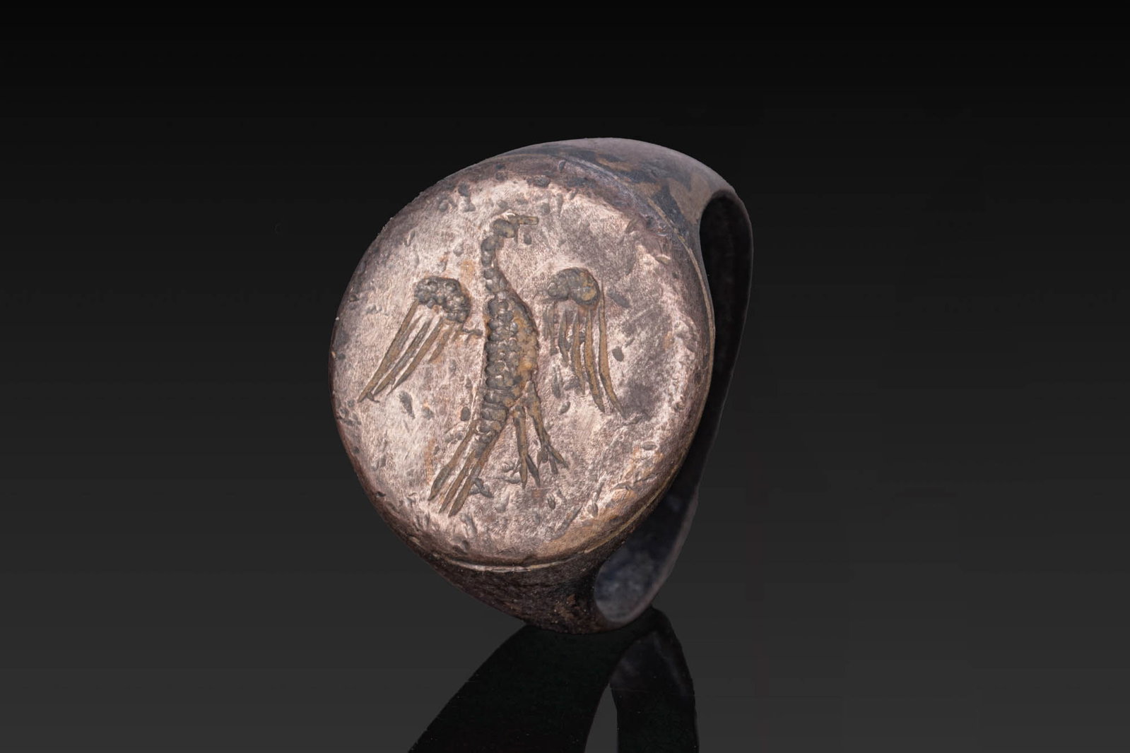 ROMAN SILVER RING WITH EAGLE: Ca. AD 1 - 300. A silver ring with a flat-section hoop widening at the shoulders and a flat circular bezel engraved with an eagle with spread wings. For similar see: The British Museum, Museum number 