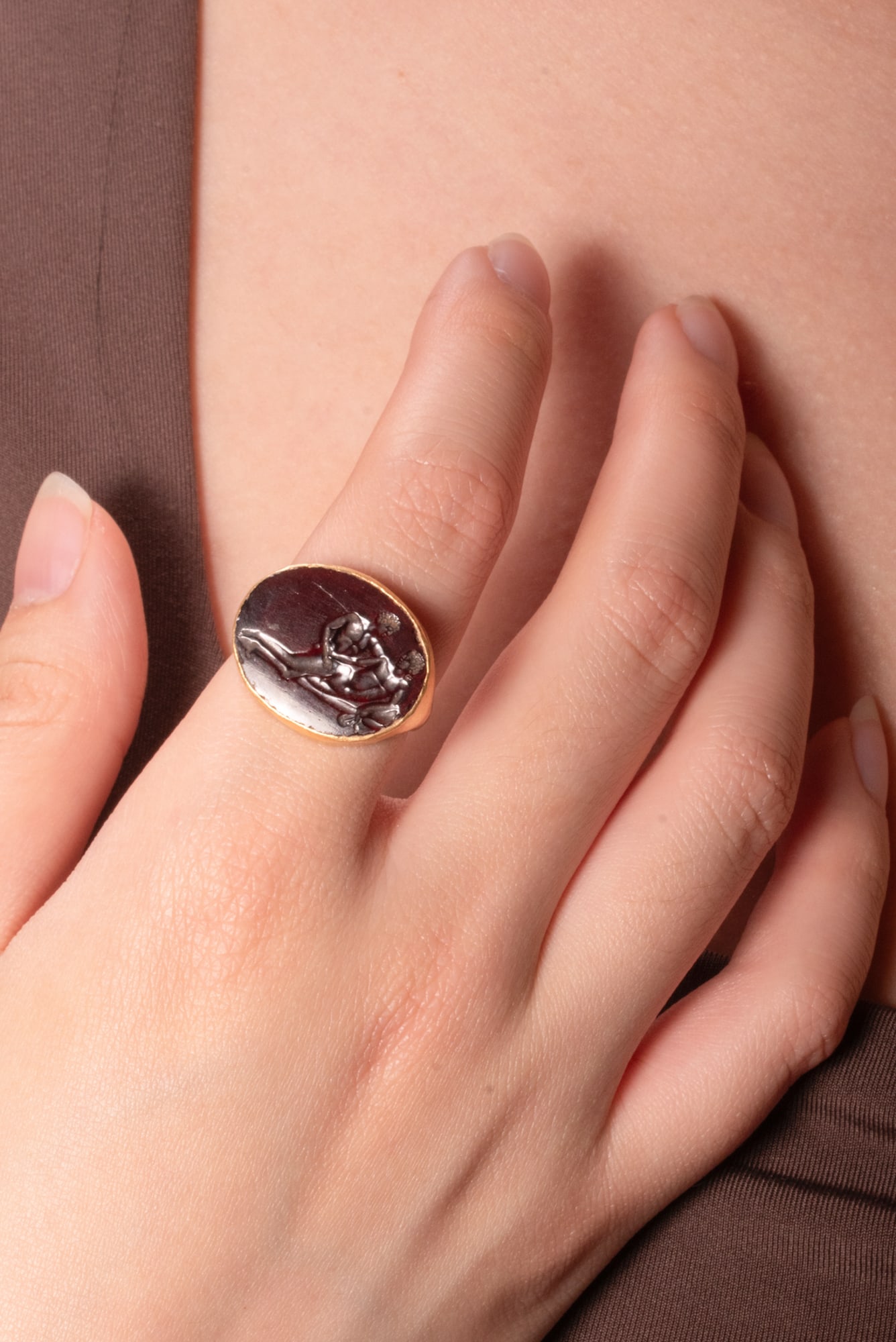 ROMAN GOLD RING WITH CARNELIAN INTAGLIO OF EROTIC SCENE: Ca. 100 BC - AD 100 (or later). A gold ring with a slender hoop expanding to a large, oval bezel set with a carnelian intaglio engraved with an erotic scene showing two nude figures reclining on a dra