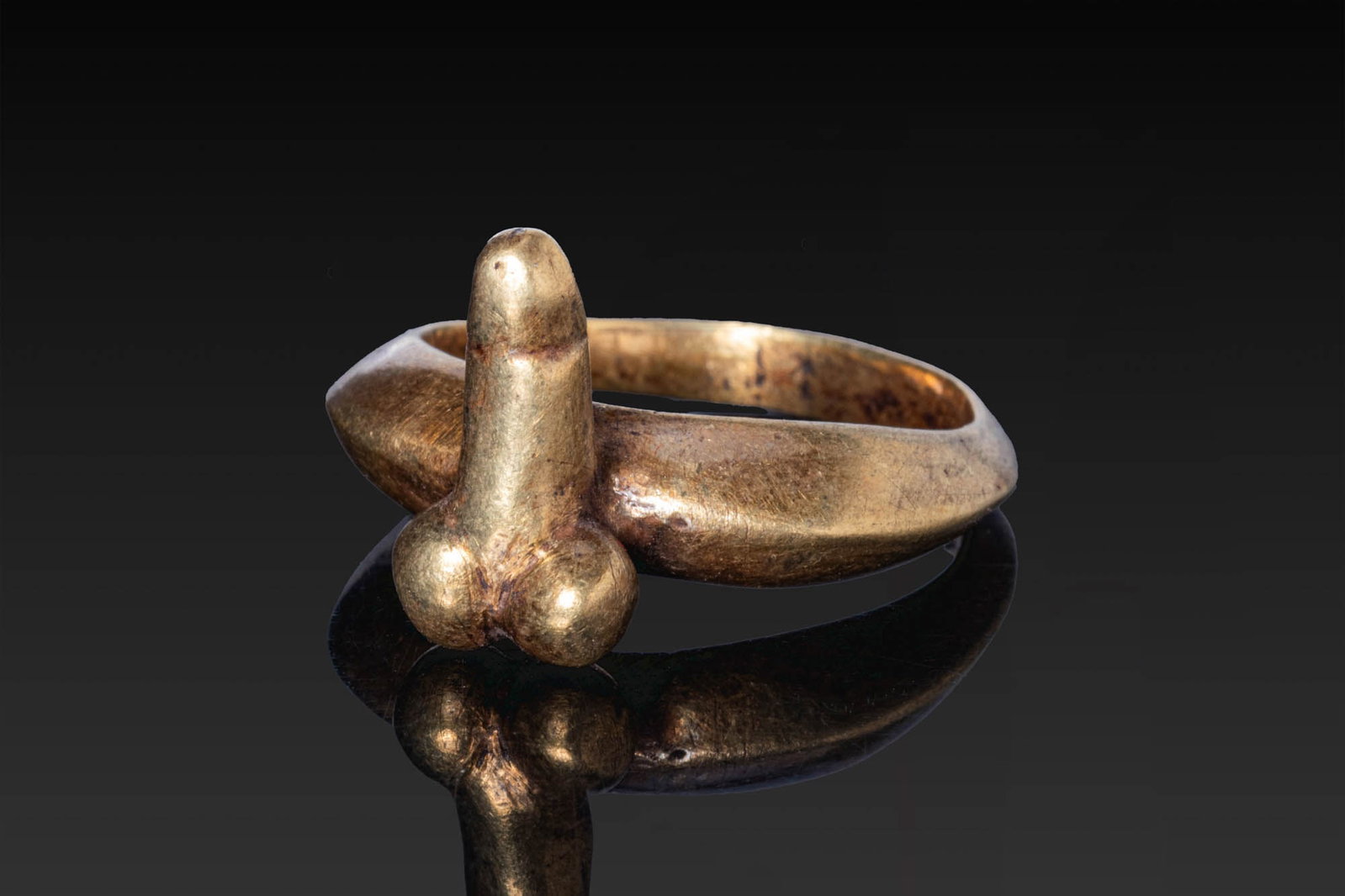 ROMAN GOLD RING WITH PHALLUS: Ca. AD 1 - 300. A gold ring with a carinated hoop tapering towards the rear and surmounted by a phallus modelled with prominent testicles. For similar see: The British Museum, Museum number 1872,0604.